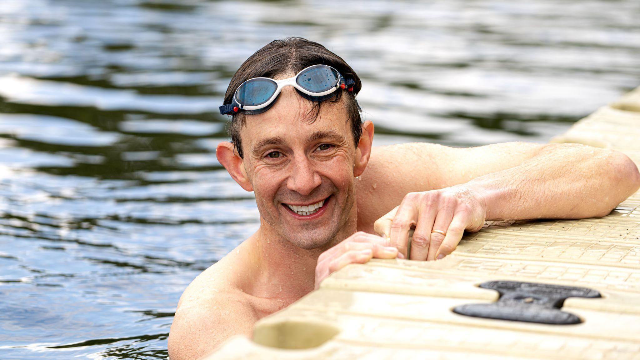 Consultant Dr Michael Carter smiling for the camera from the edge of a pool. He is wearing goggles on his head.