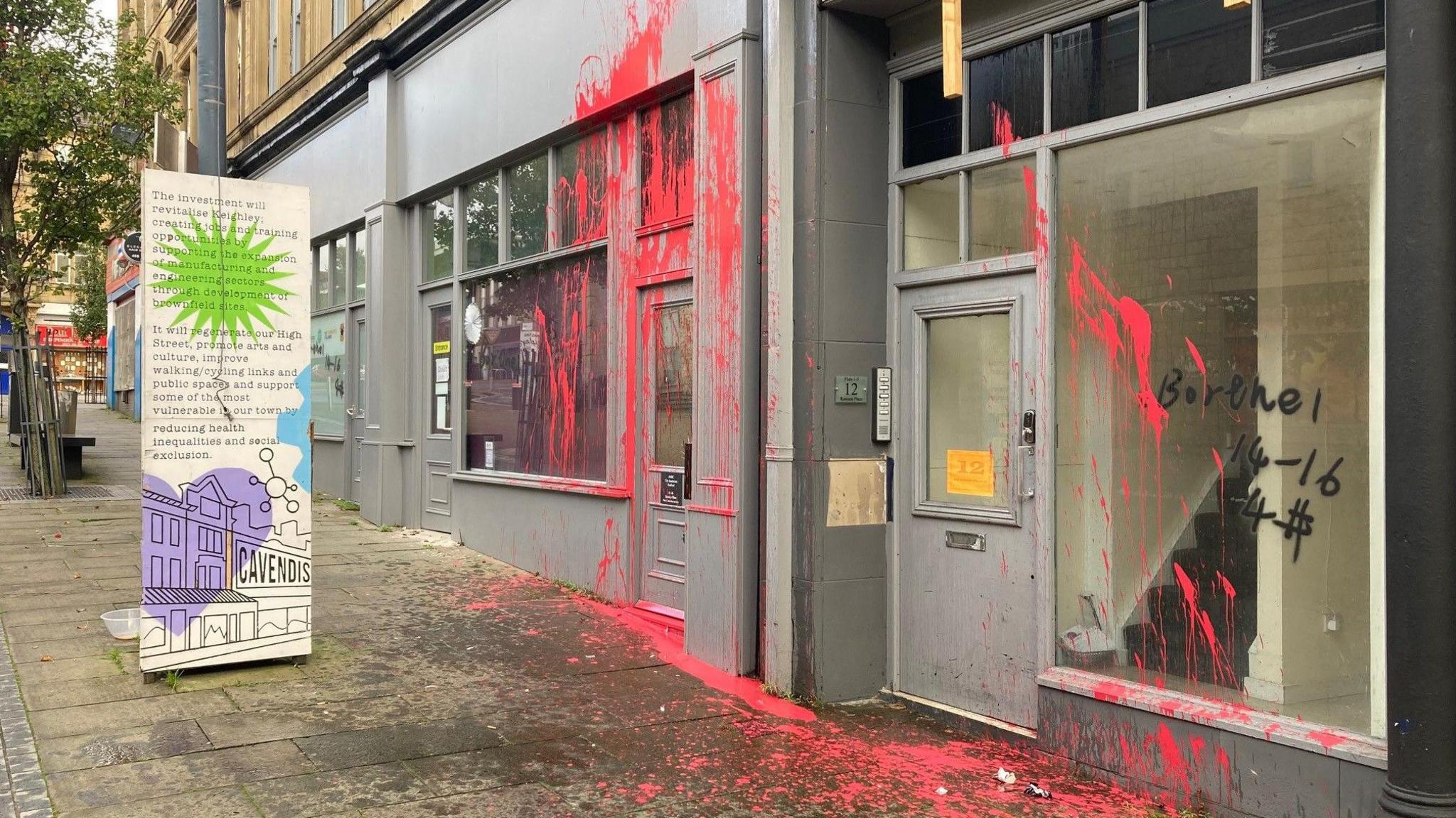 Two grey-coloured shop fronts covered in red paint with the pavement also spattered.