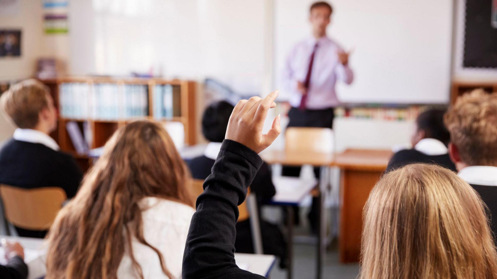 A pupil with her hand up in a school classroom