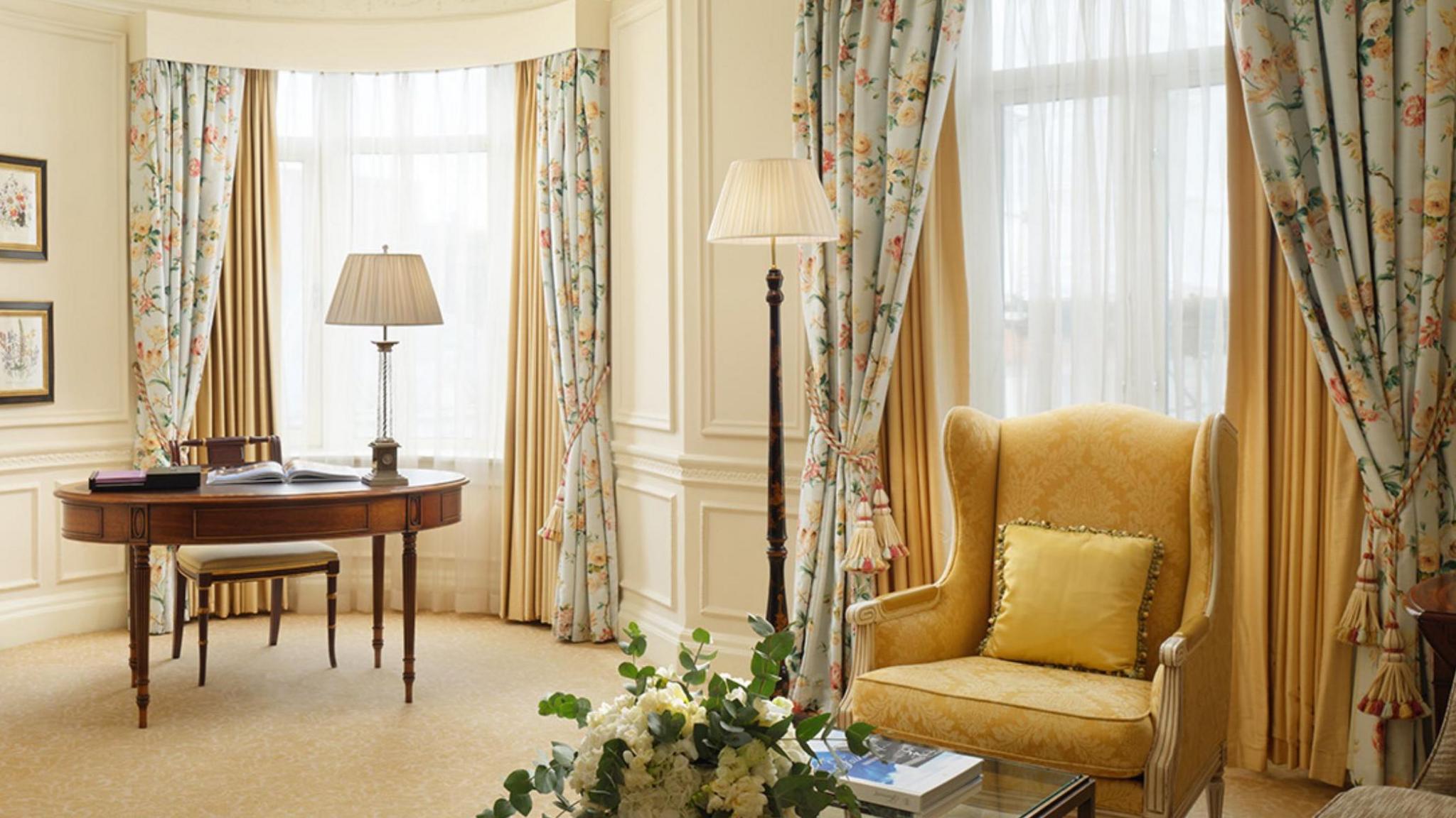 A room inside The Savoy with floral curtains, a wooden desk and yellow armchair.