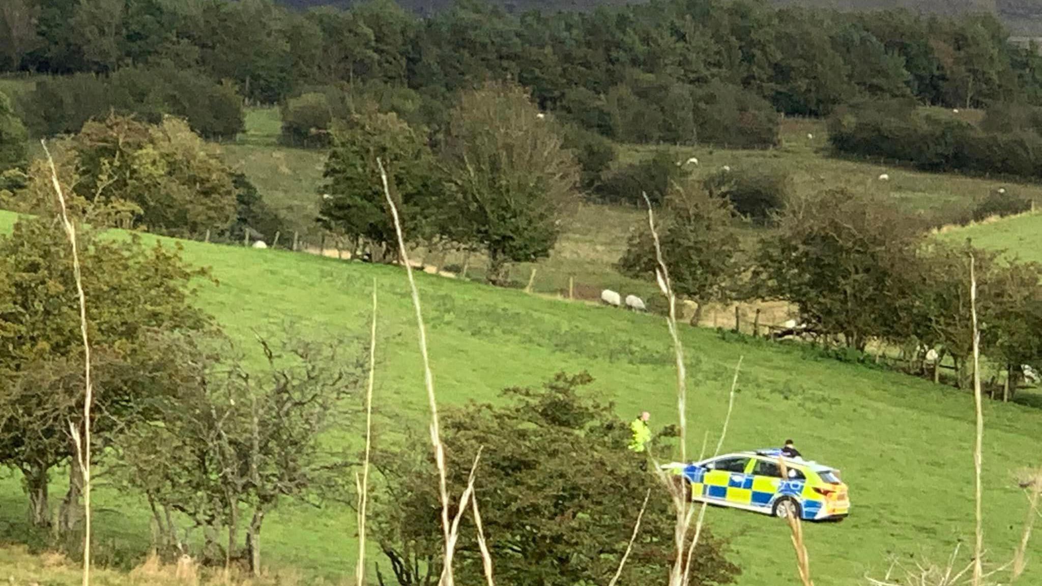 A police car and two officers on a field near Warcop in Cumbria where the child was injured