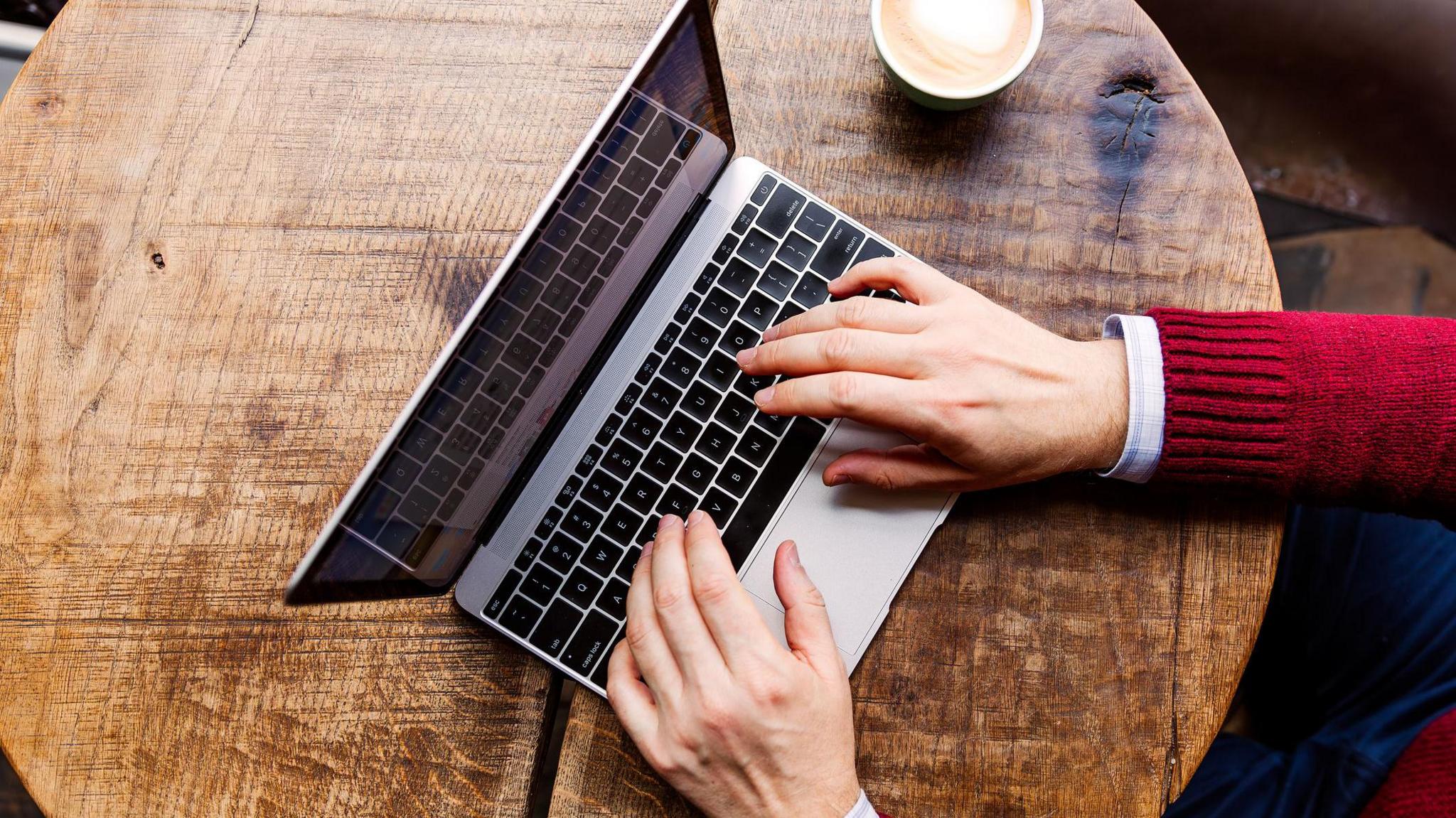 Làmhan air coimpiutair-uchd air bòrd le cupa cofaidh