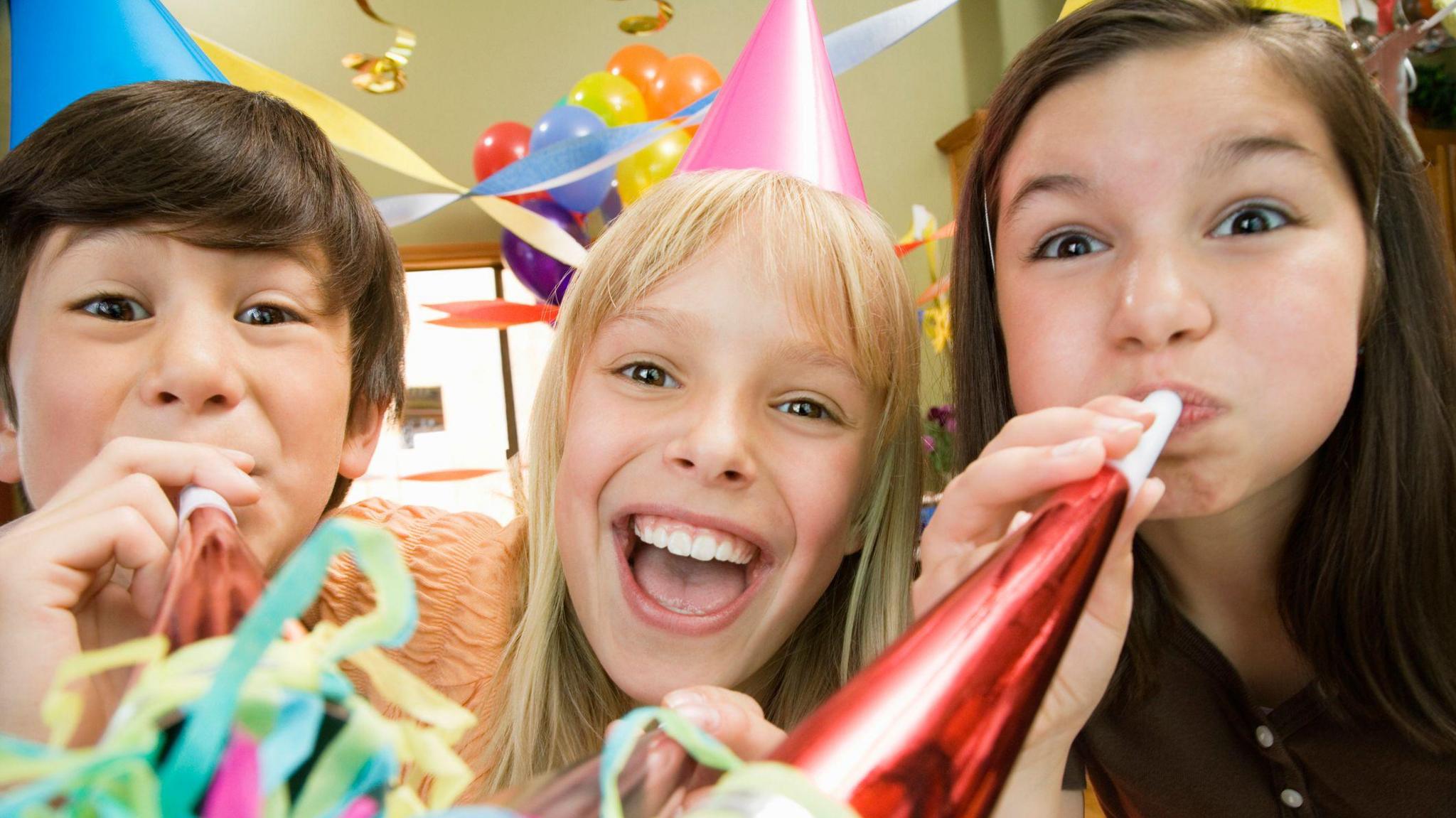 Three kids blowing noise makers at birthday party.
