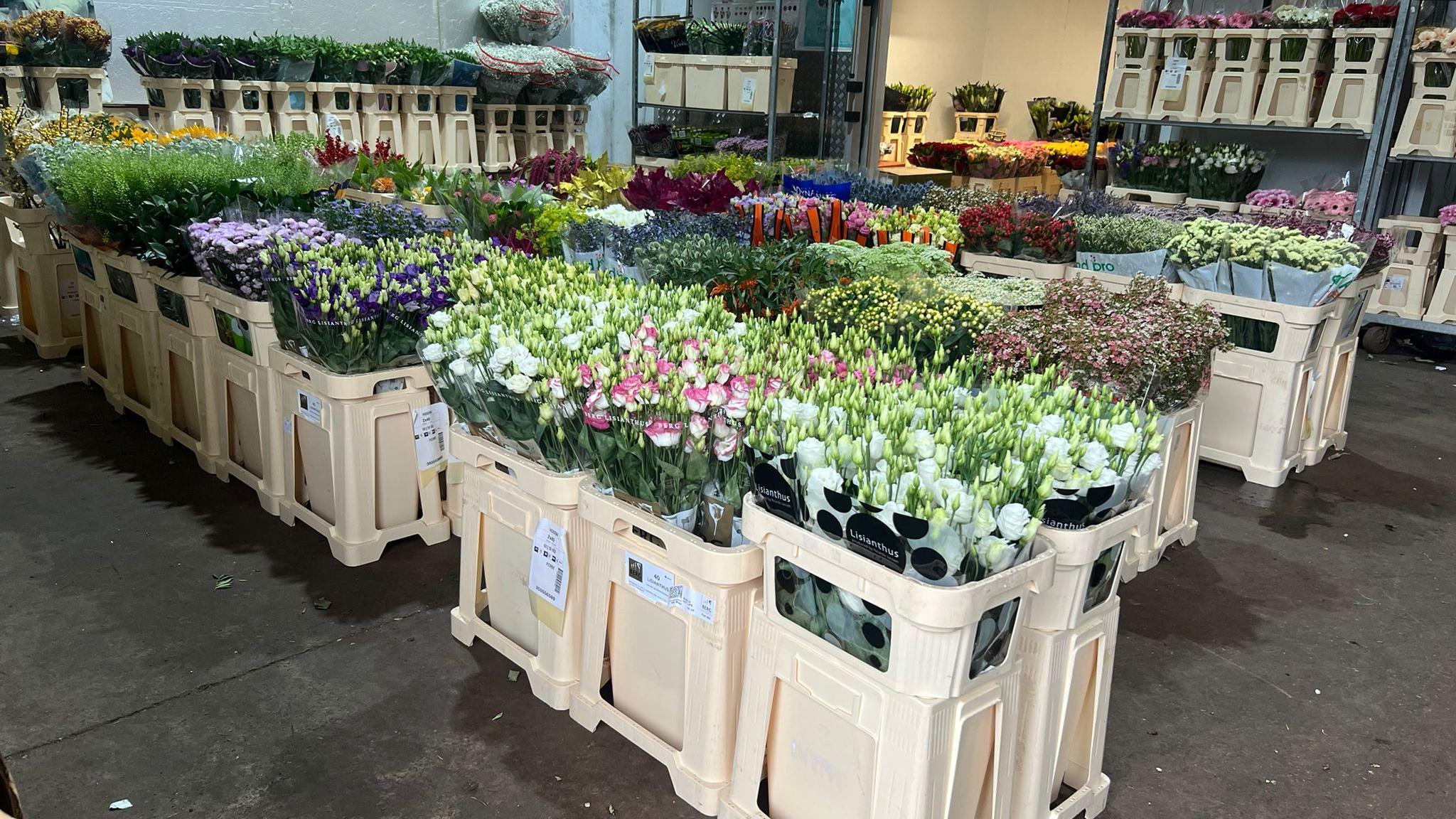 The Flower Market stall at Wolverhampton Wholesale Market, with crates on the concrete floor holding bunches of flowers in different colours and shelving in the background.