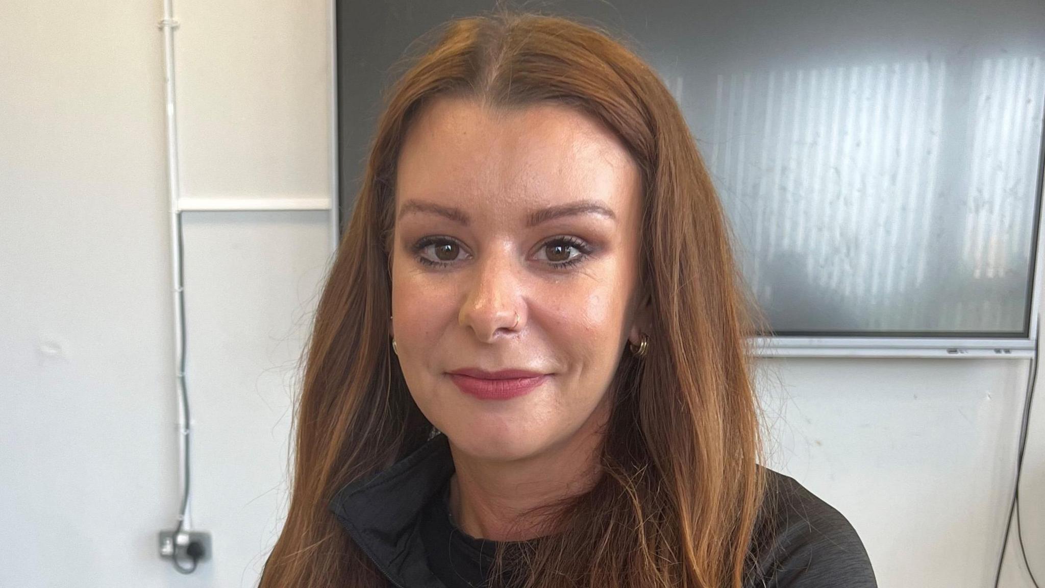 A head and shoulders shot of Seana McConville who has long brown hair. She is wearing a dark top and has pink lipstick.