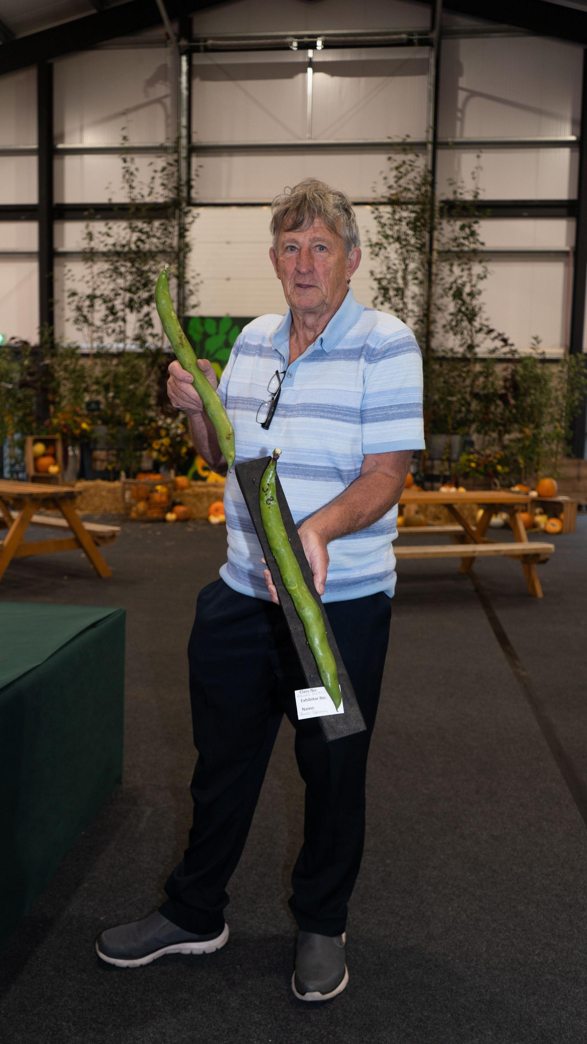 A man stands in a warehouse type building, holding up two large beans. 