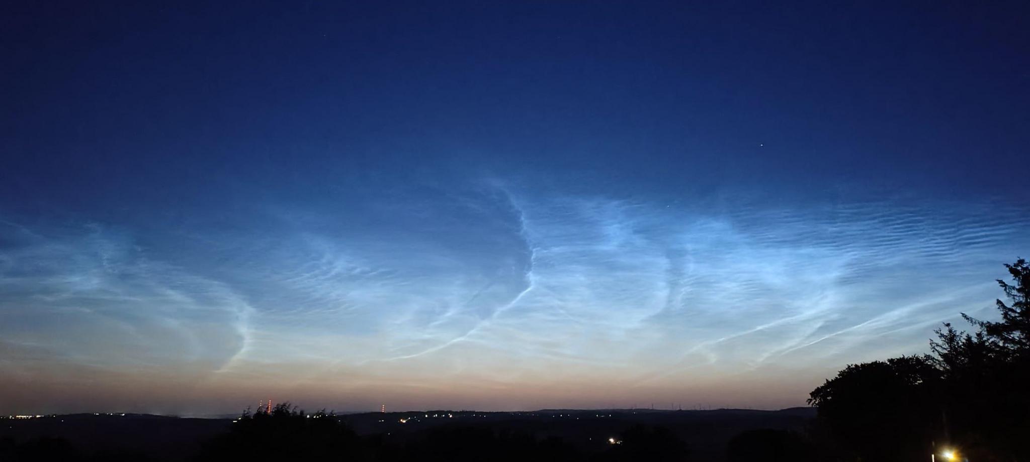The streaky blue and silver clouds appear against a sky pink and dark blue in colour. The lights of houses show faintly in the darkness.