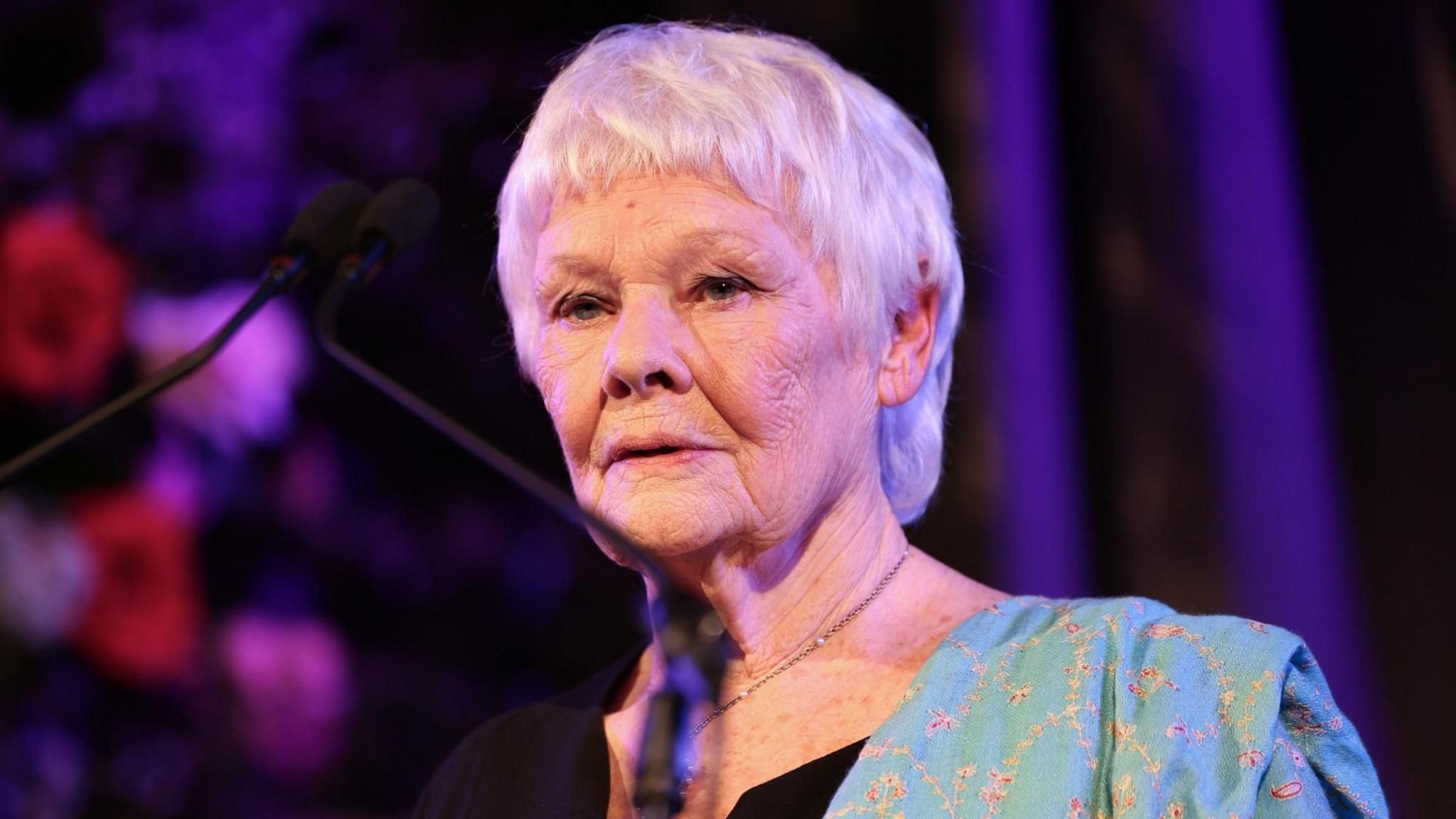 Dame Judi Dench performs on stage at a Celebration of Shakespeare event at Grosvenor House, central London. There is purple lighting behind her, and she has a sad expression on her face