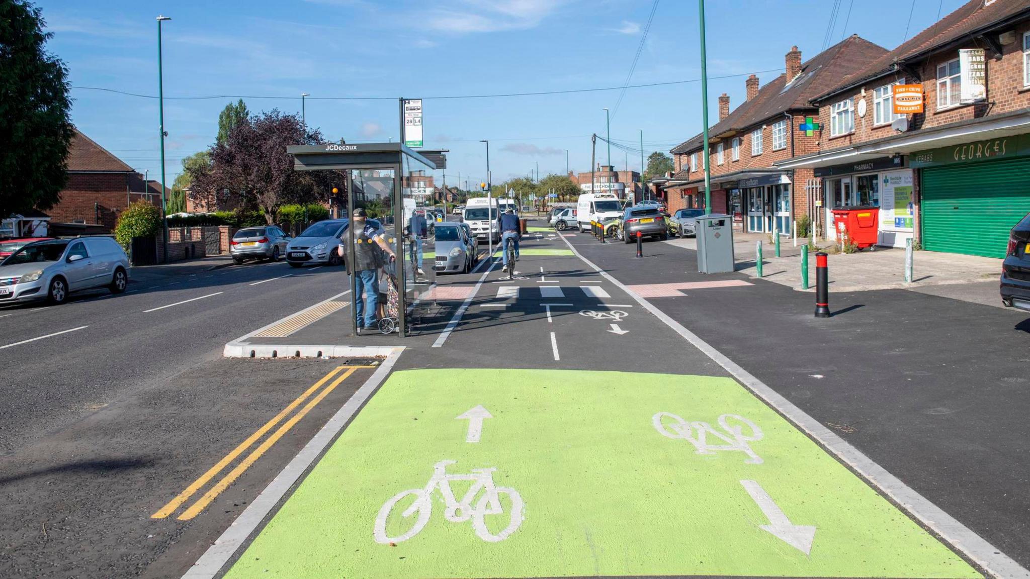 New two-way cycle lanes in Nottingham next to a road. A bus stop can be seen to the left with a row of brick building shops and homes to the right.