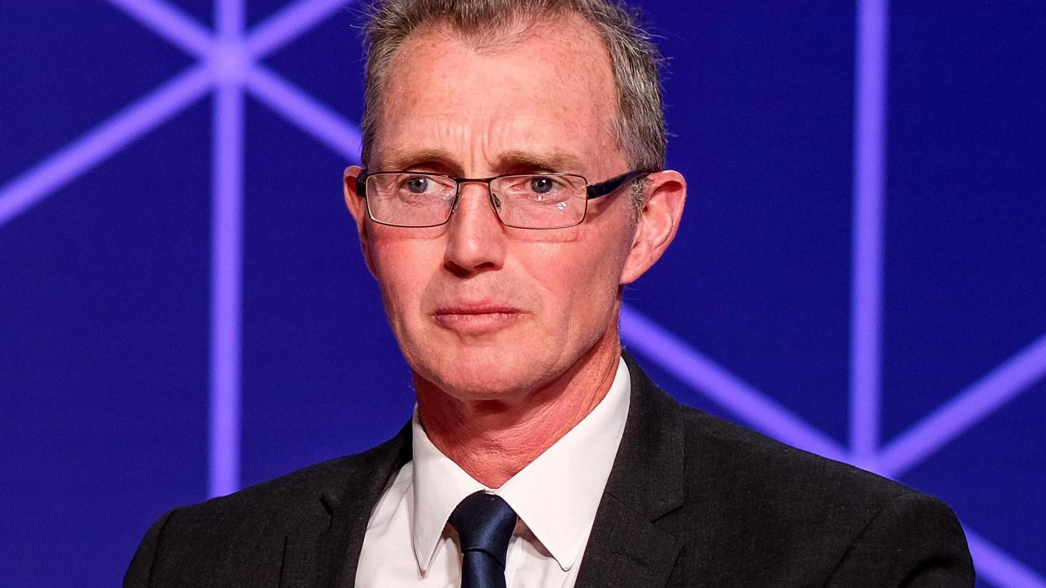 David TC Davies sat in a ˿ studio, wearing a tie, suit and glasses.