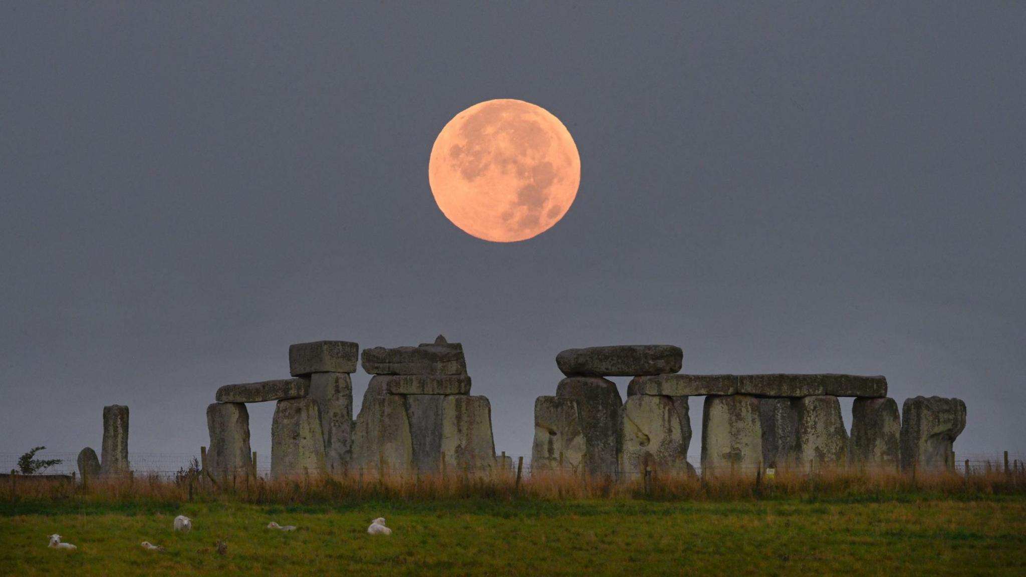 The super harvest moon rises over the ancient stone circle at Stonehenge, Wiltshire, UK.