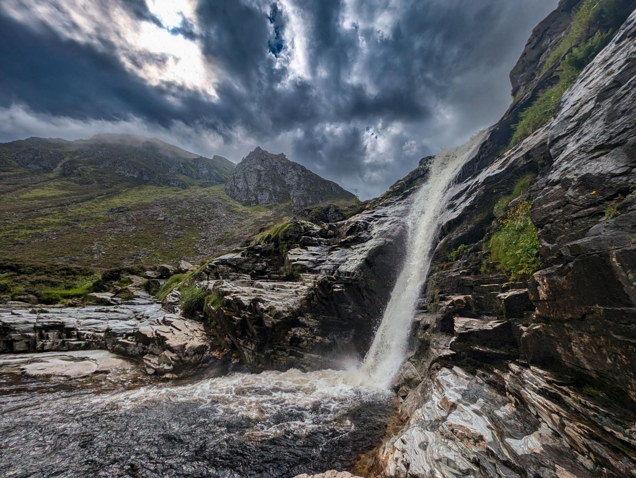 Flowing waterfall over jagged grey rocks under a dark blue and grey sky