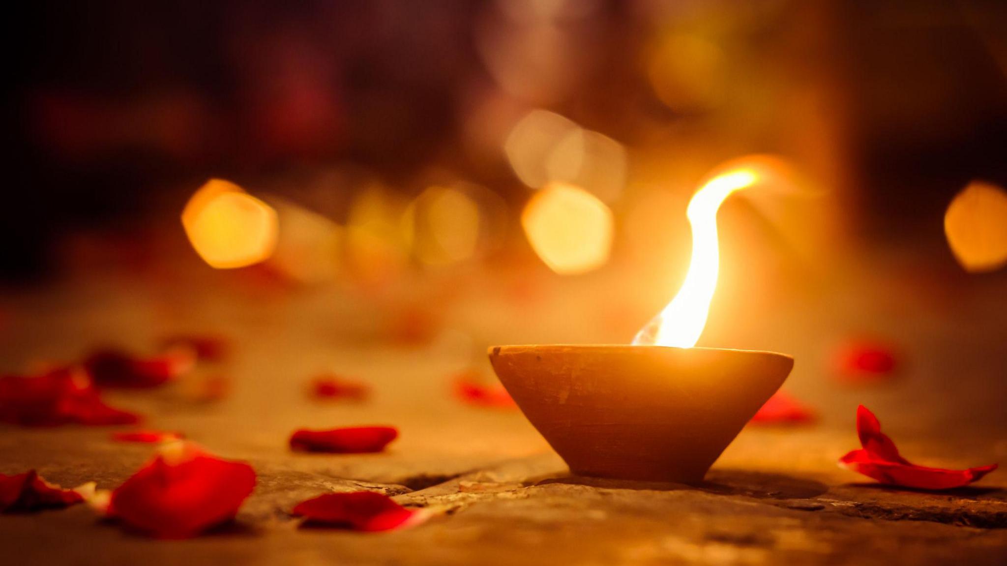 Diya lamp surrounded by rose petals.