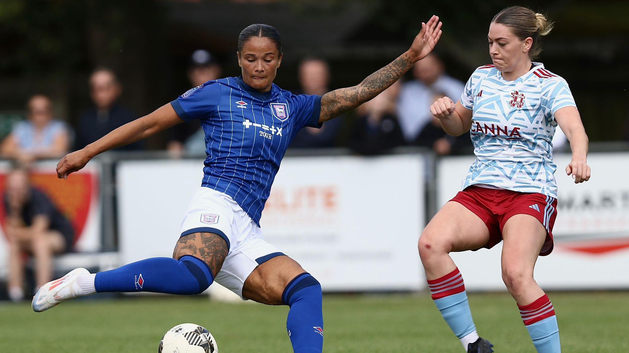 Ipswich Town Women's striker Natasha Thomas, in her blue Ipswich Town kit, preparing to strike the ball, closed down by Hastag United's Courtney Lumley, in a claret and blue away kit. 