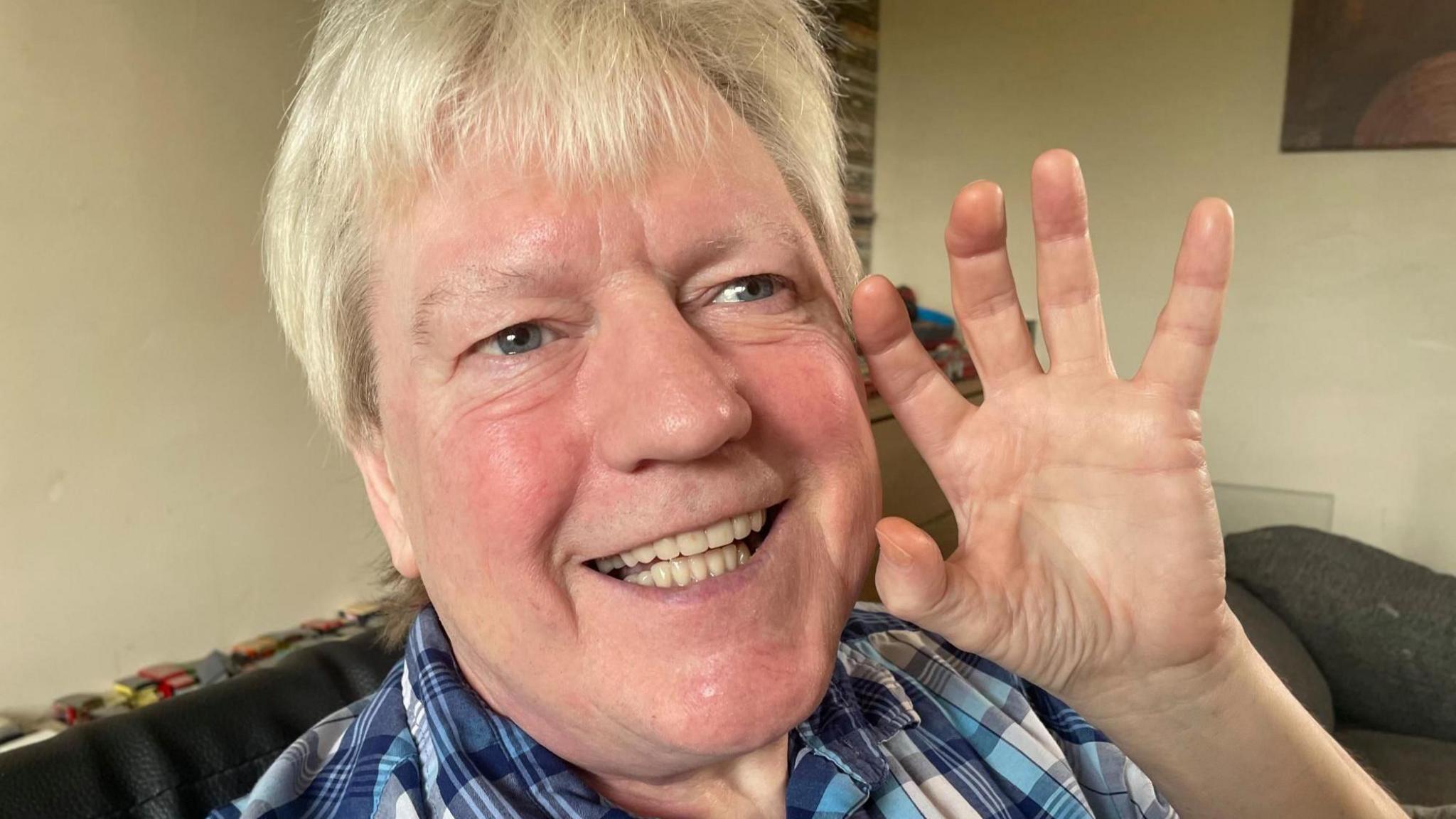 A middle aged man holds his hand up to his mouth, showing off his white teeth,