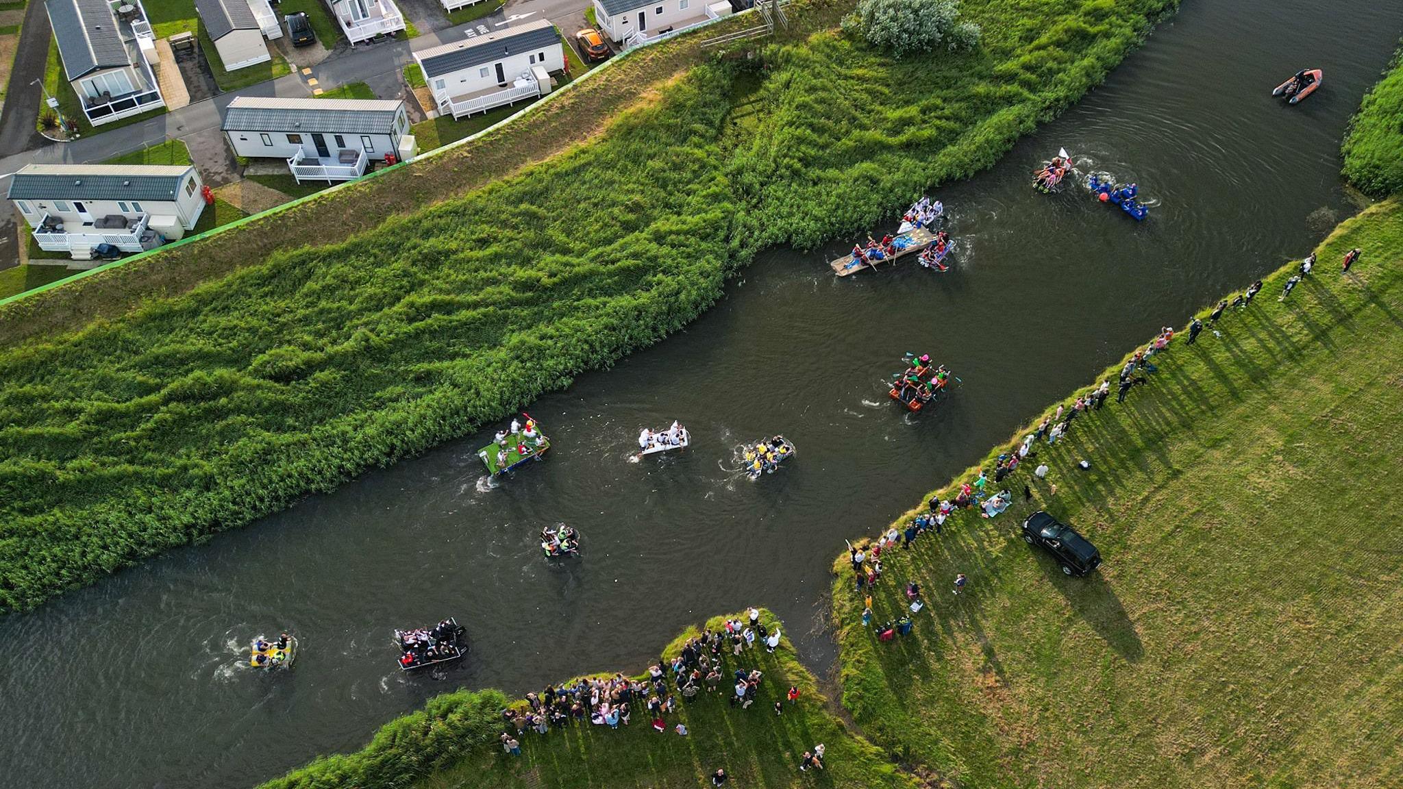 People in fancy dress and homemade rafts drifting down a river