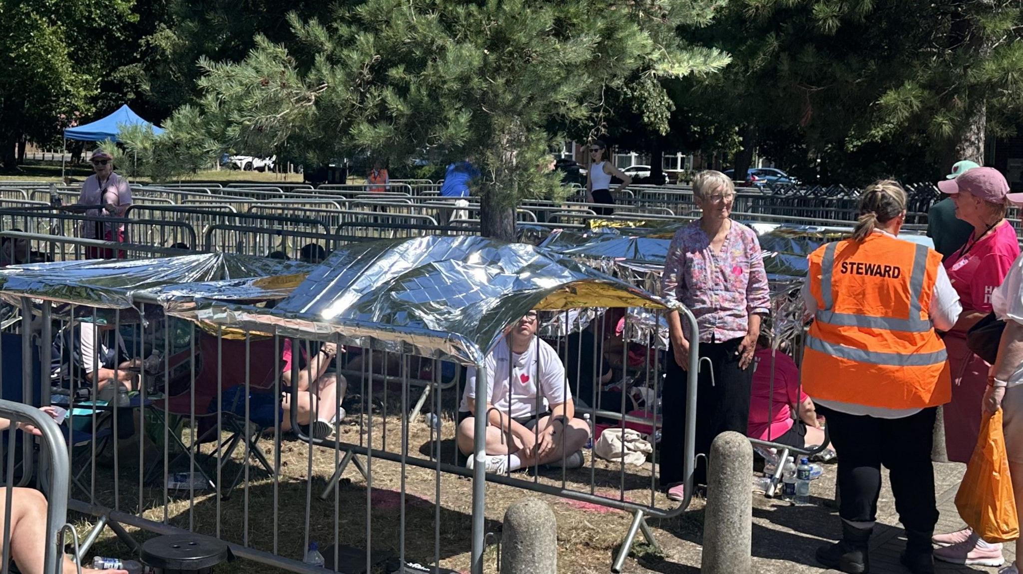 Fans sit on the ground within lines of metal gates with foil blankets resting above them to provide shade.