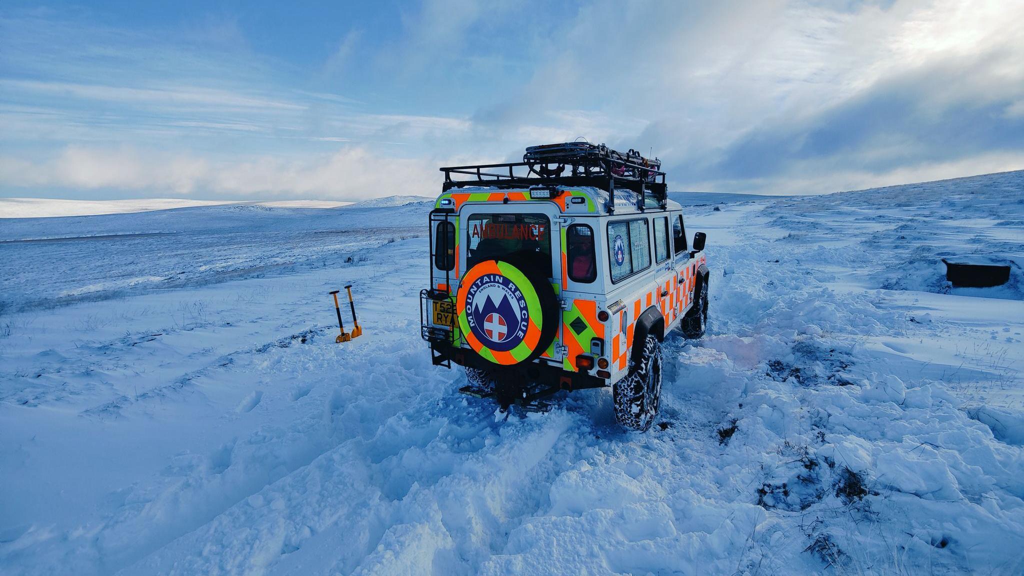 The search and rescue team's Land Rover photographed from the rear. It is surrounded by snow and there are two spades stock in to a snow drift.