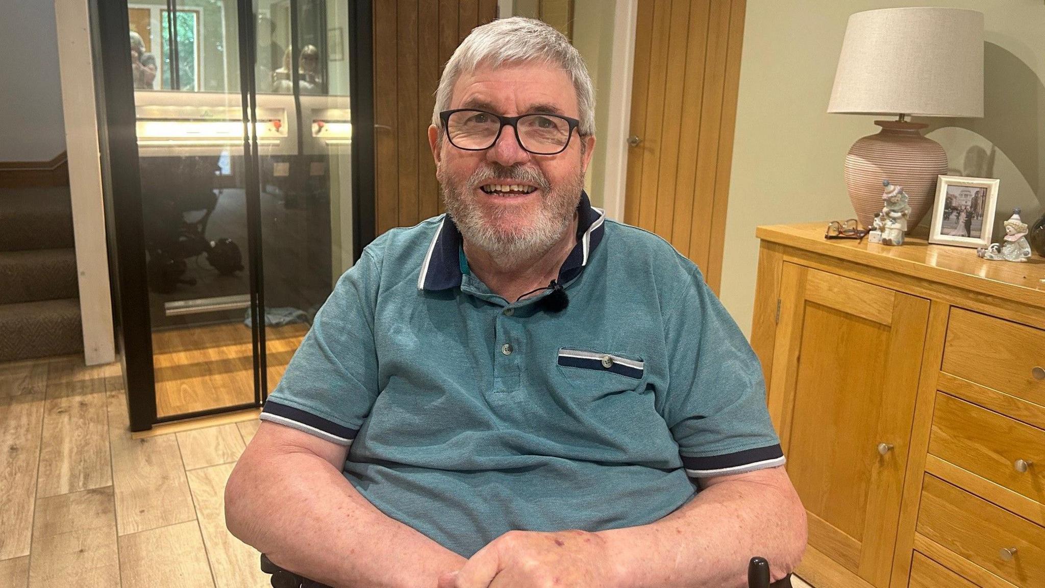 A man in a wheelchair wearing a green polo shirt and glasses