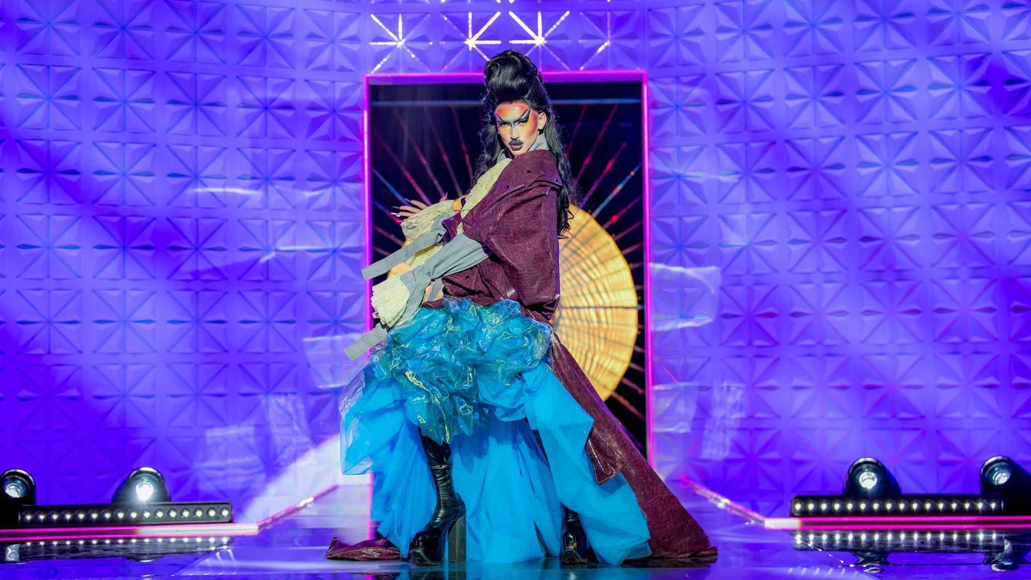 Kyran Thrax walking the Drag Race UK runway in a purple and blue gown