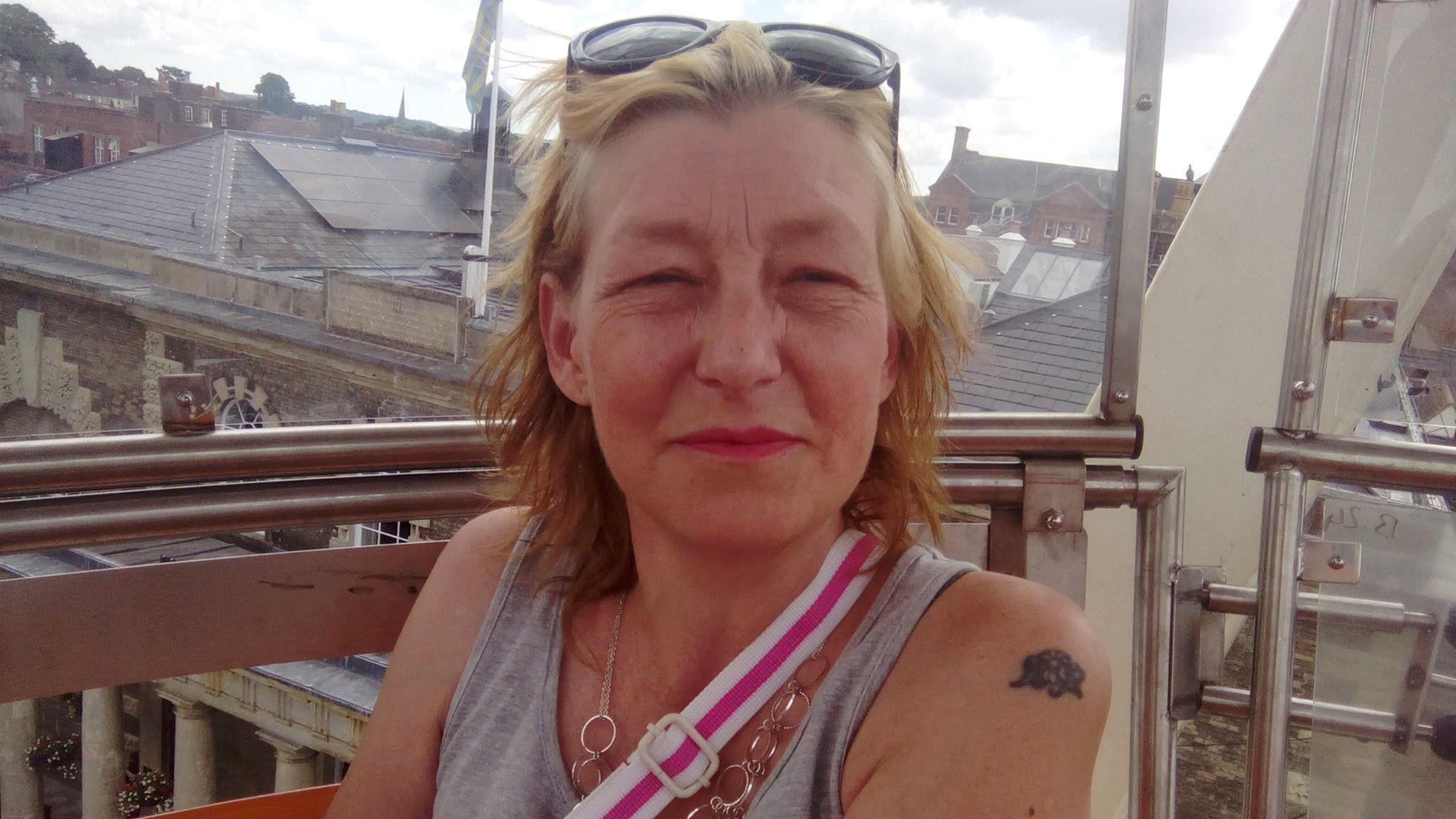 44-year-old Dawn Sturgess is pictured smiling on a balcony wearing a grey vest, crossbody bag and sunglasses on her head.