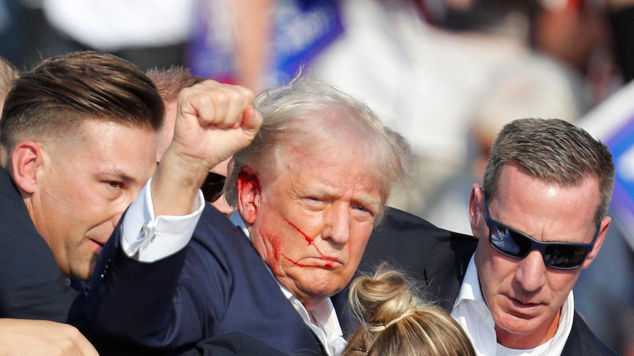 Donal Trump punches the air with blood running down his face