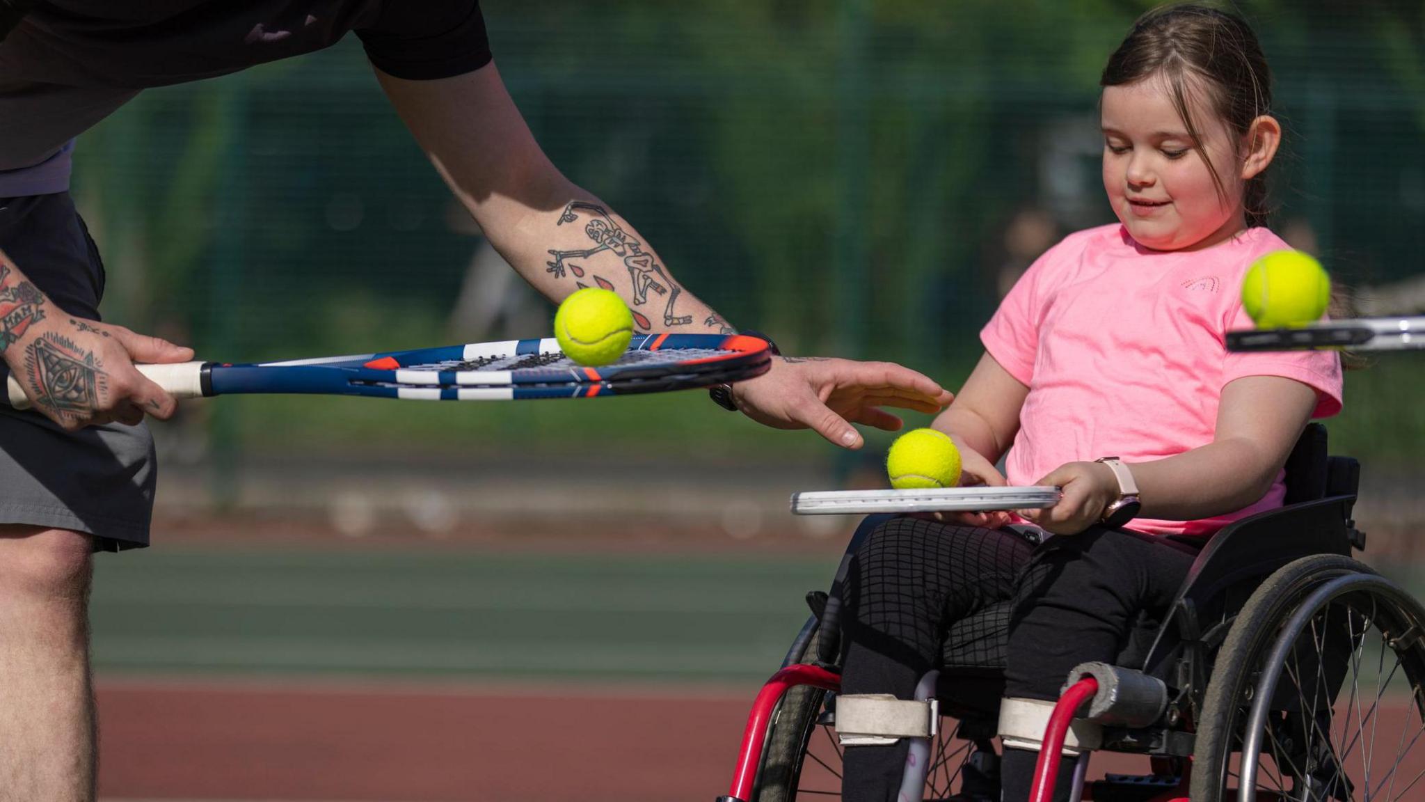 disabled child being taught how to play tennis, in a wheelchair