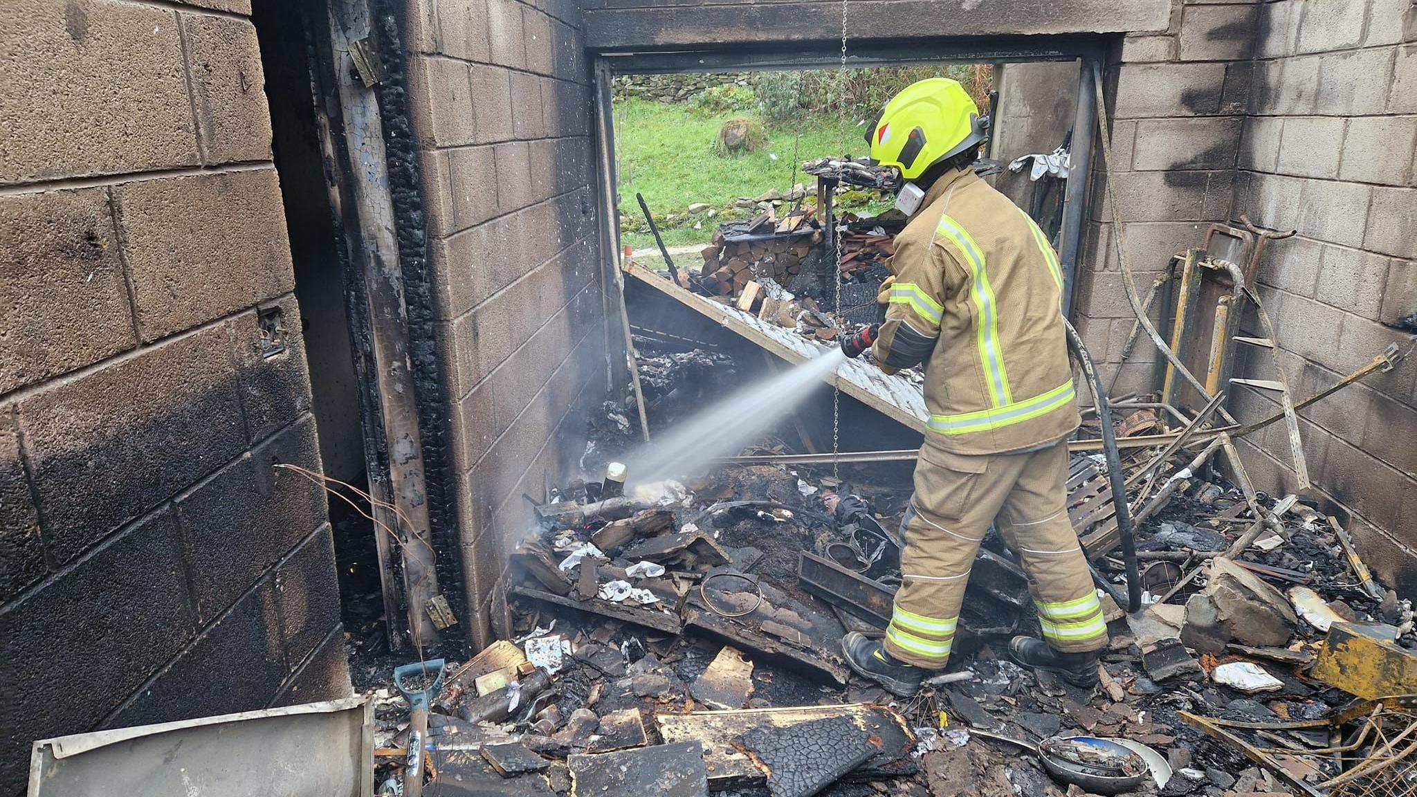 A firefighter sprays water towards the floor in a burnt-out house.