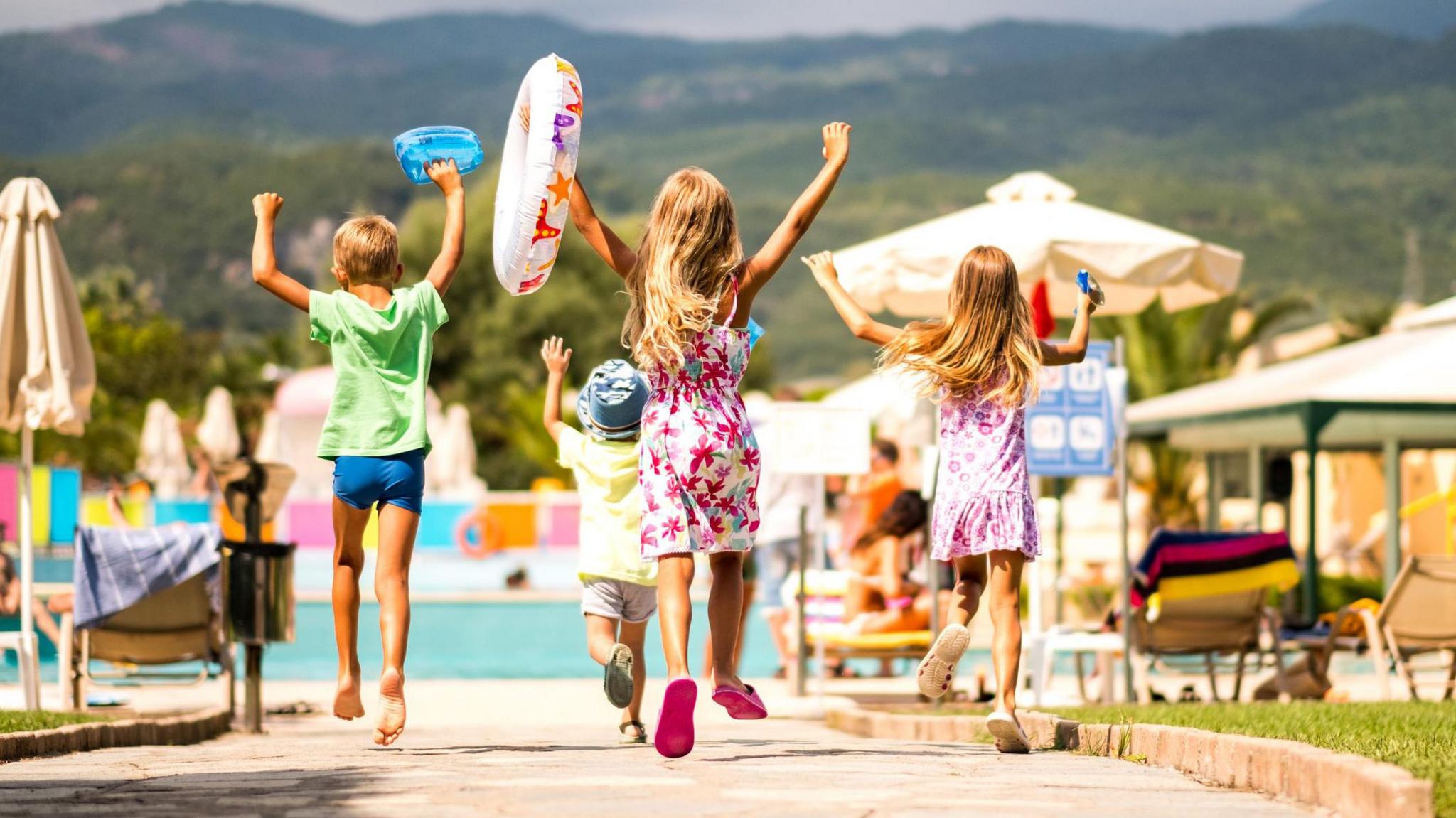 A group of children head towards a swimming pool on holiday.