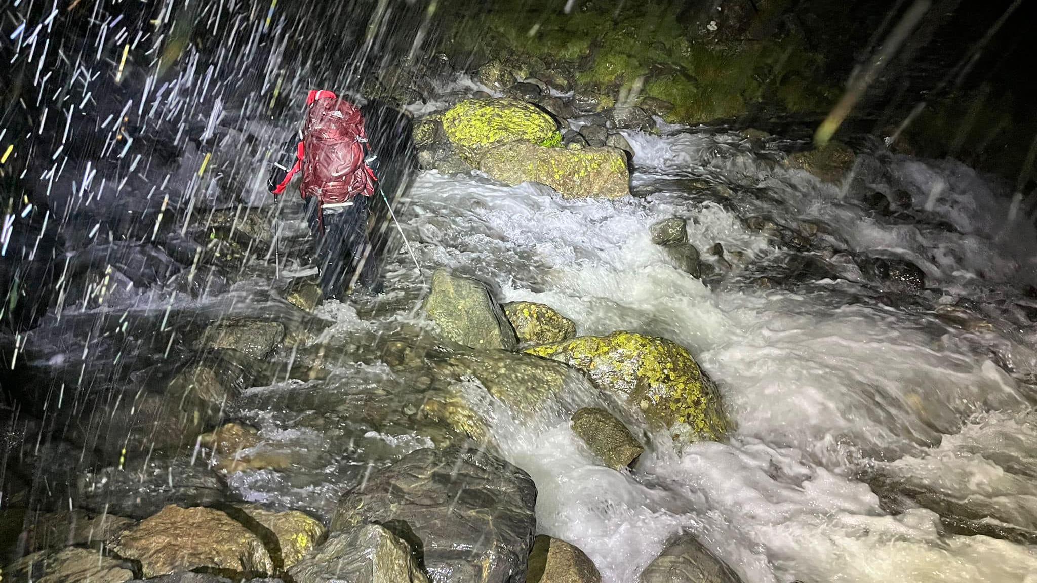 Mountain Rescue volunteers pick their way across a swollen and dangerous gully where the stream has flooded.