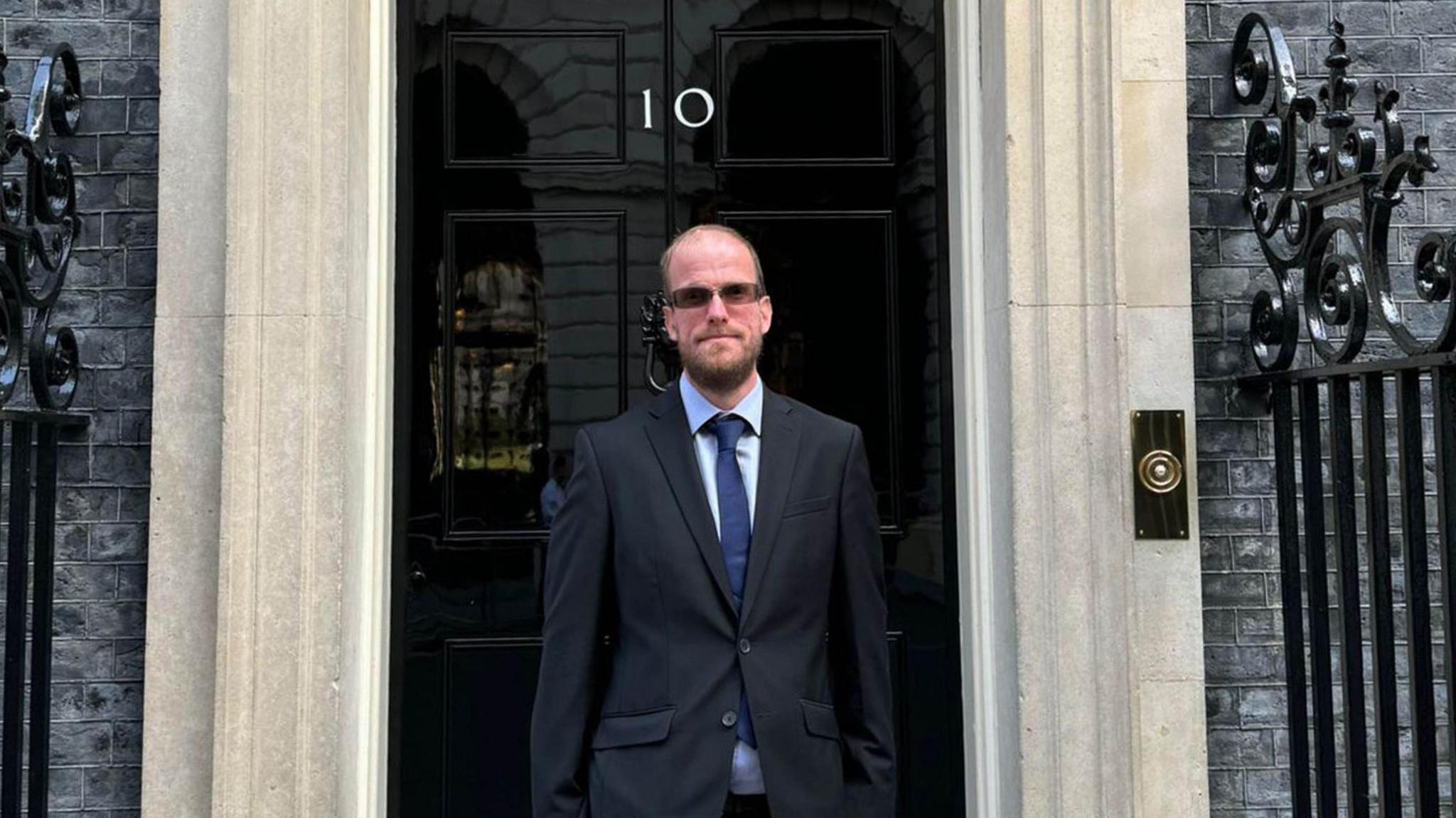 Mr Dye outside Number 10 Downing Street. He wears a black suit and blue tie.