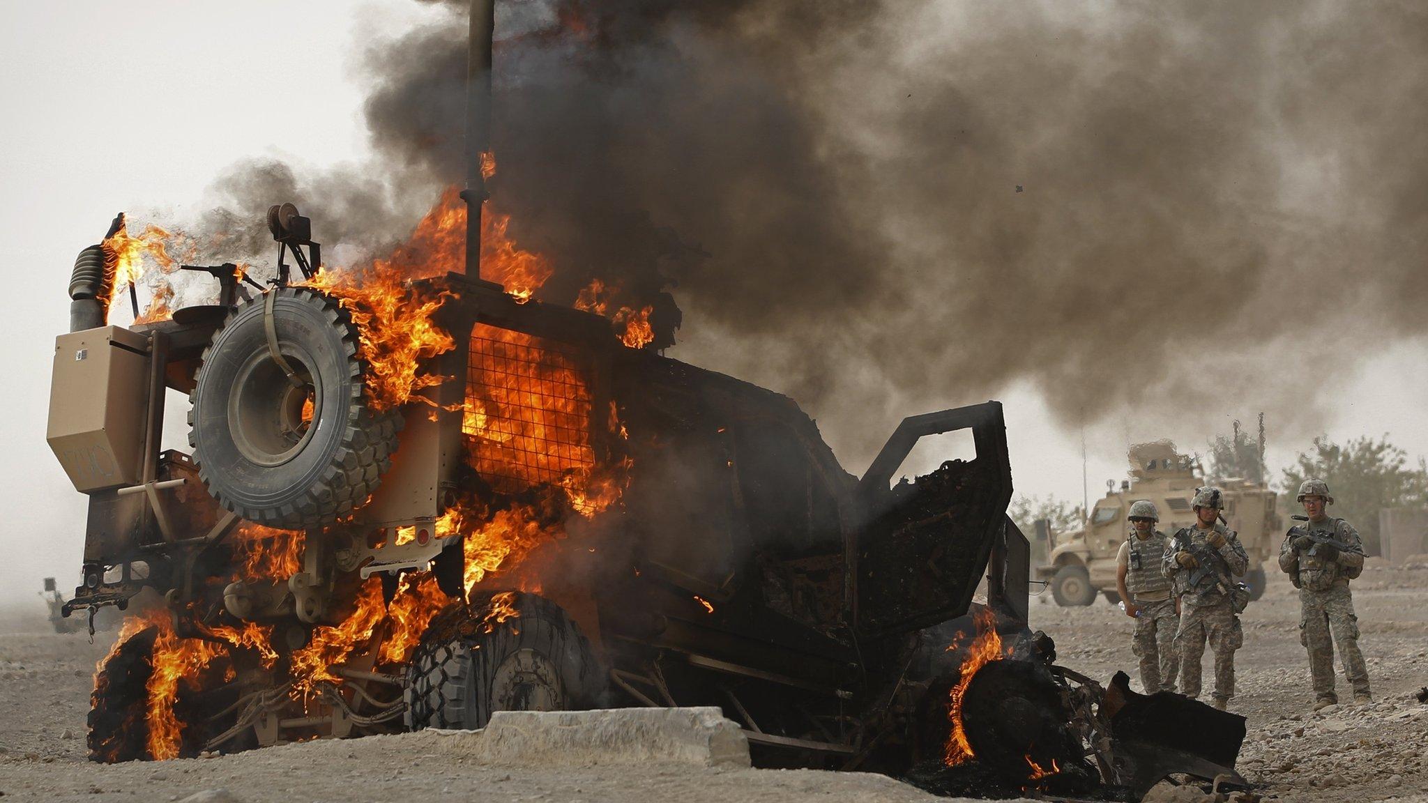 Us soldiers watch as an armoured vehicle burns