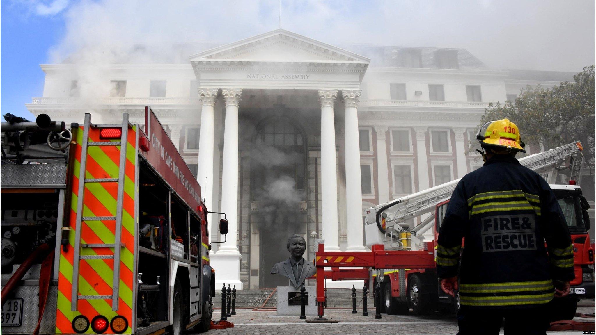 A firefighter and a fire engine are seen in front of the parliament building in Cape Town, South Africa, as smoke emerges from the door (2 January 2022)