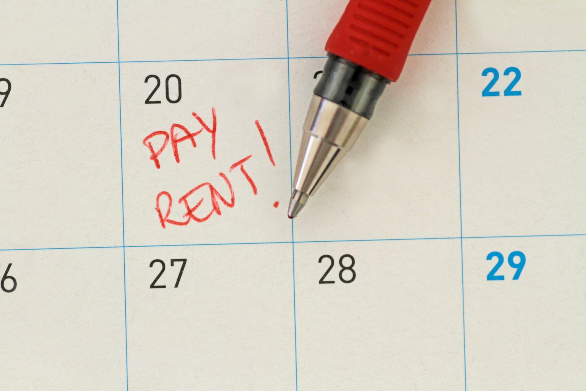 A close up of part of a calendar. PAY RENT has been written in red pen, which is resting next to the writing, on the 20th date