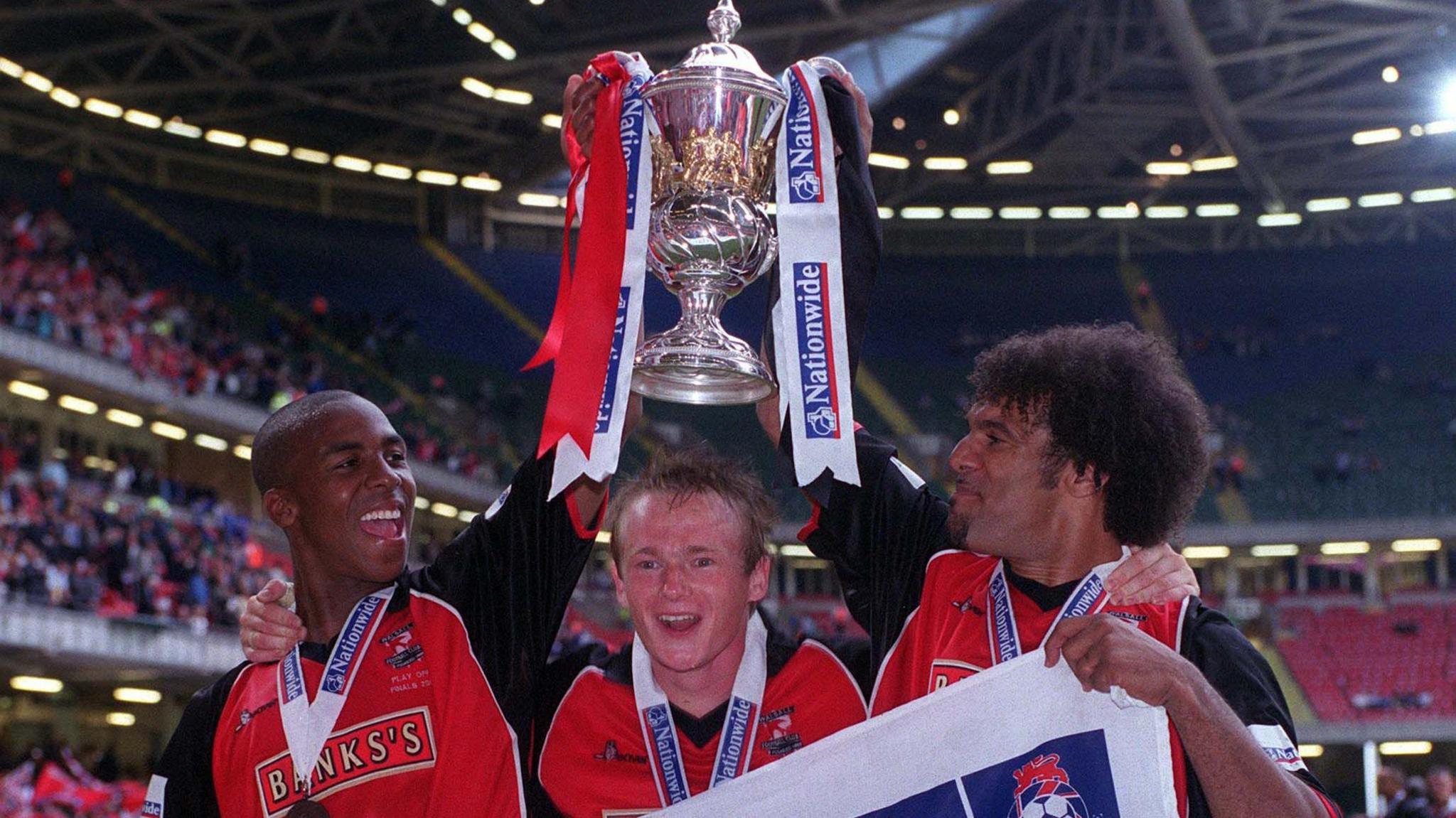 Darren Byfield (left) celebrates with team-mates and the Division Two play-off trophy in Cardiff