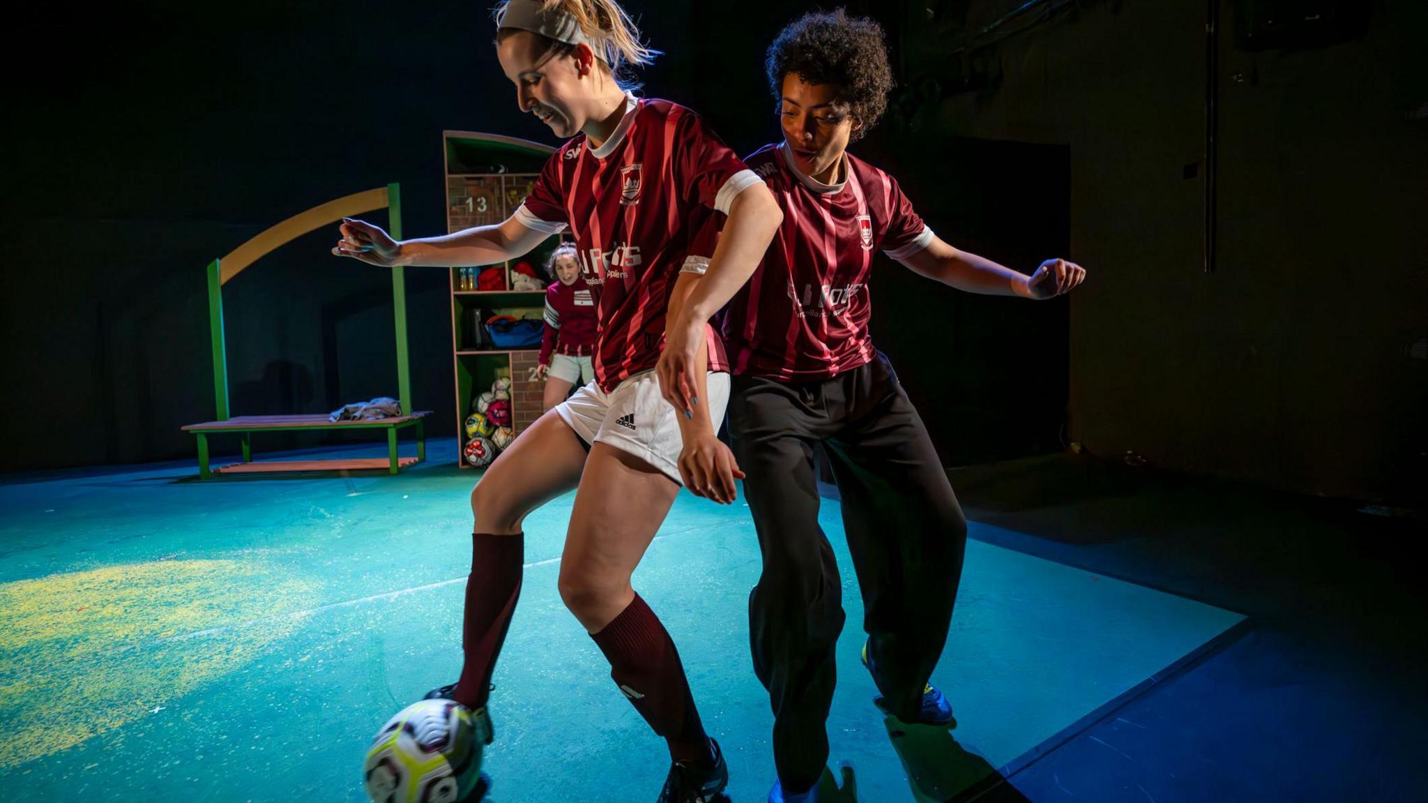 Two women back to back as they tackle a football on stage