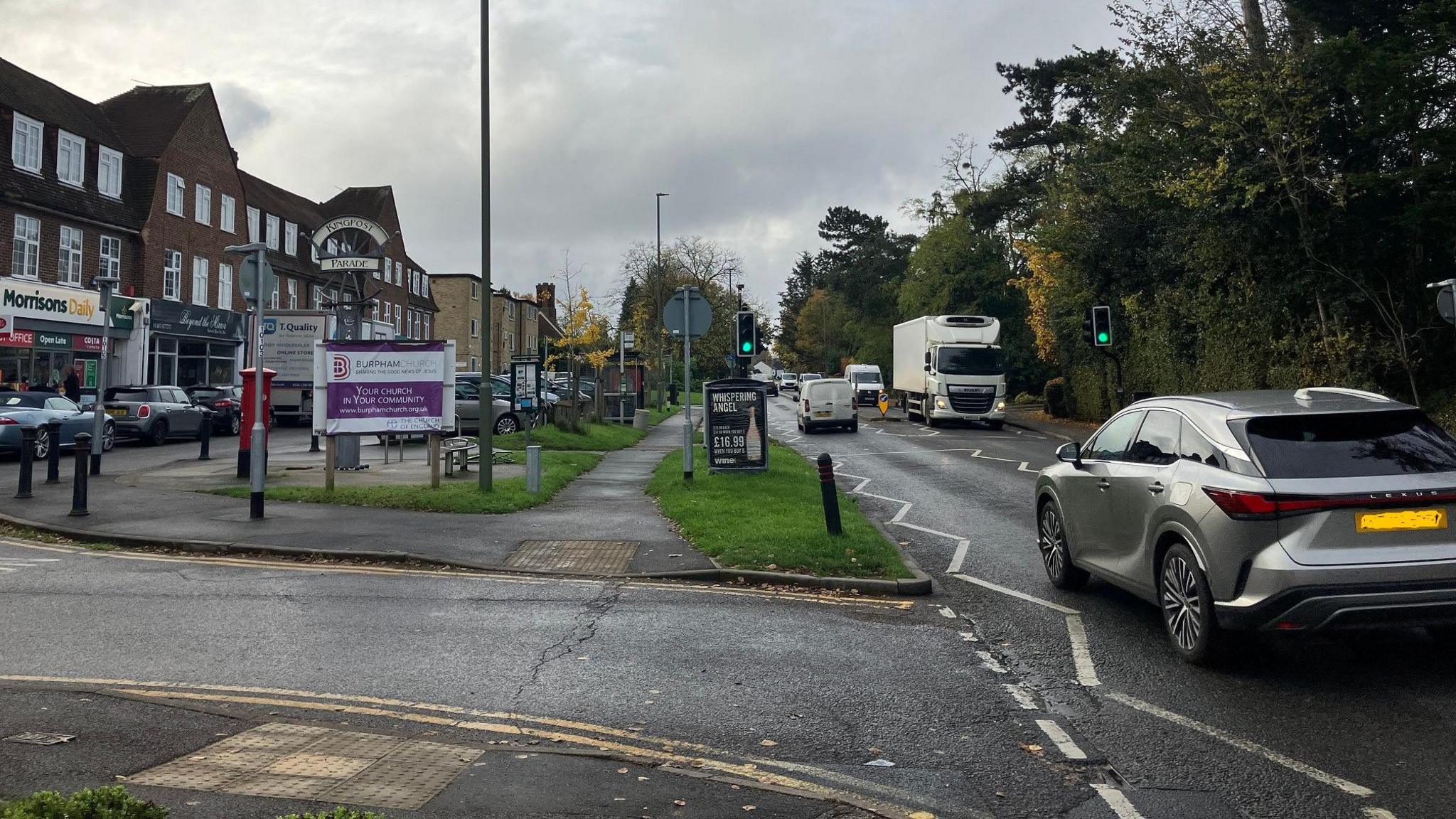 Kingspost parade of shops in Burpham on London Road, cars and other vehicles driving along the road.