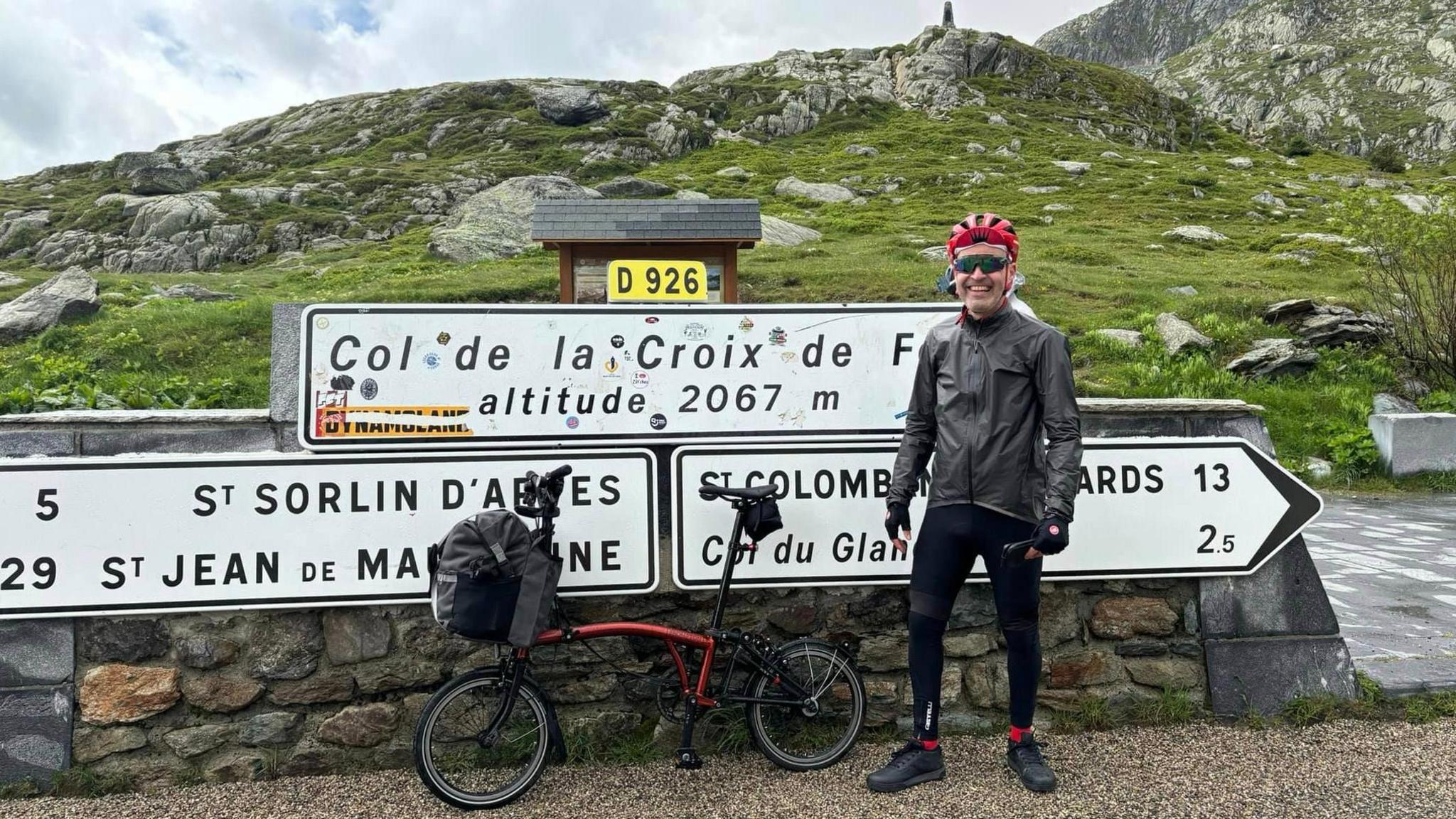 a man smiling with a foldable bike in front of signs