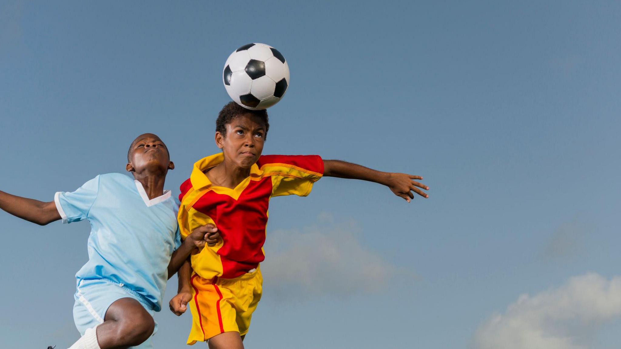 Two young boys go to header a football.