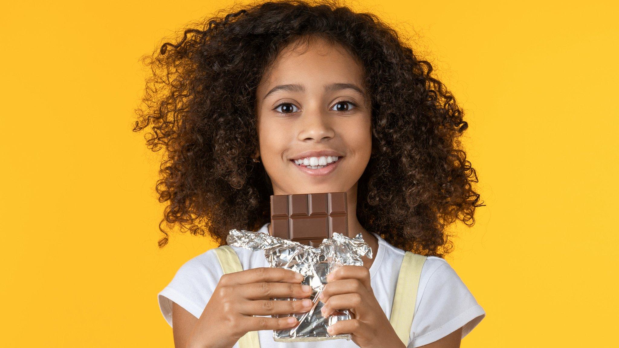 Child holding unwrapped chocolate bar.