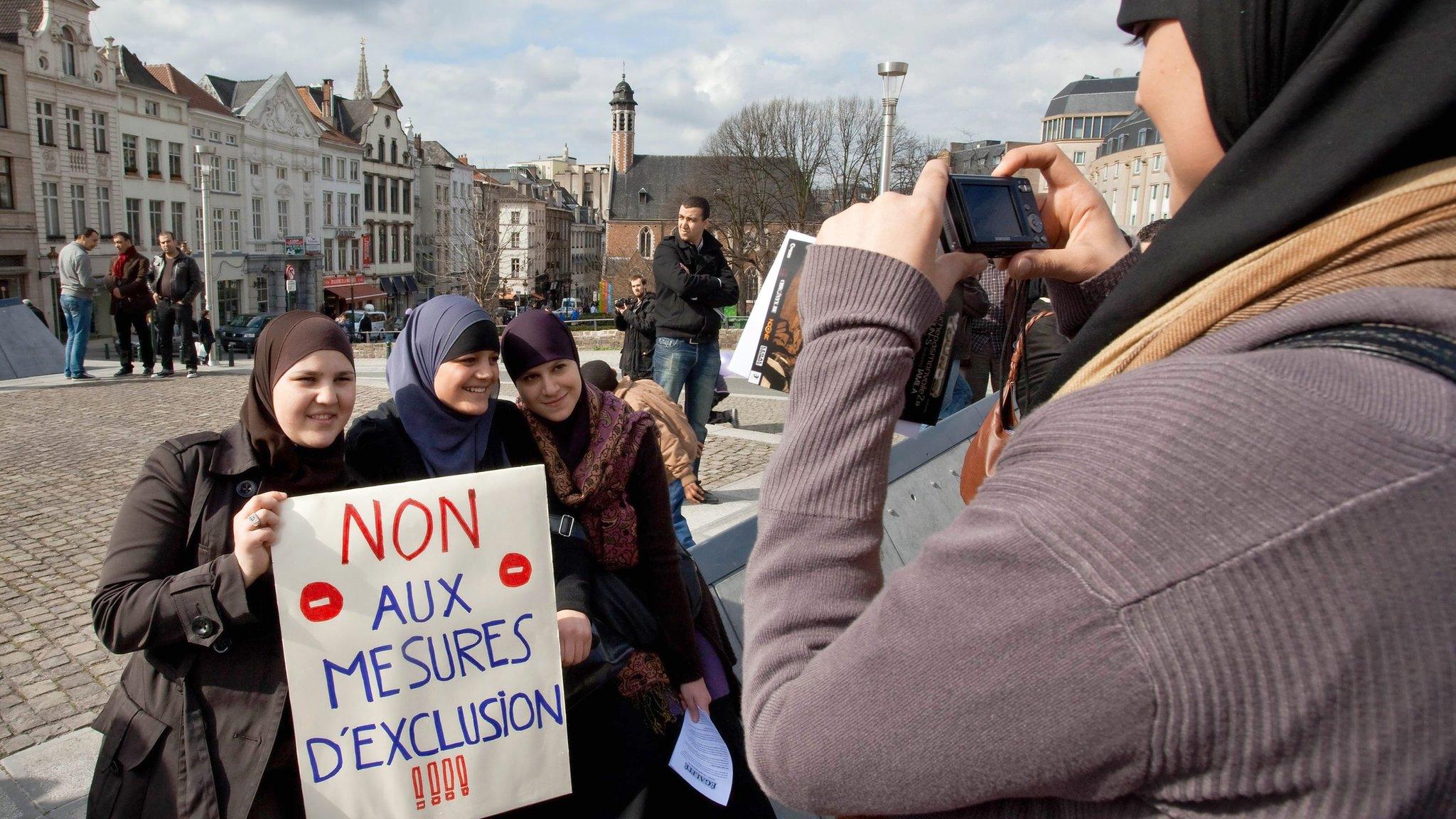 Woman takes picture of demonstrators holding placard, reading: 'No to exclusion measures,' during protest on March 27, 2010 in Brussels against prohibition of Muslim headscarf in schools