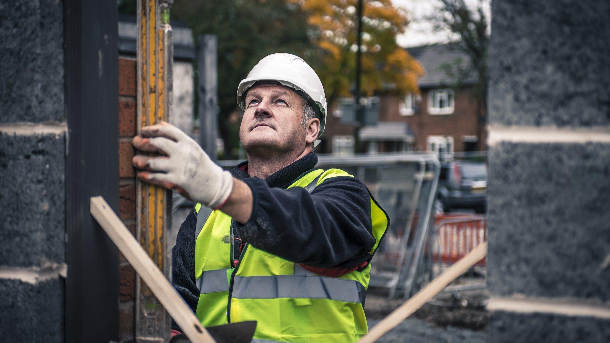 A builder in a high-vis jacket levelling bricks