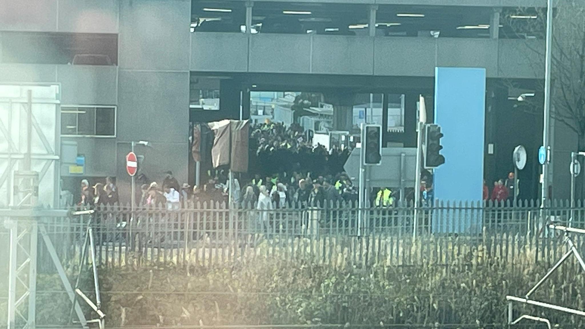 Image shows hundreds of people leaving Birmingham Airport. Some have bright yellow jackets on and are herding people out of the emergency exits