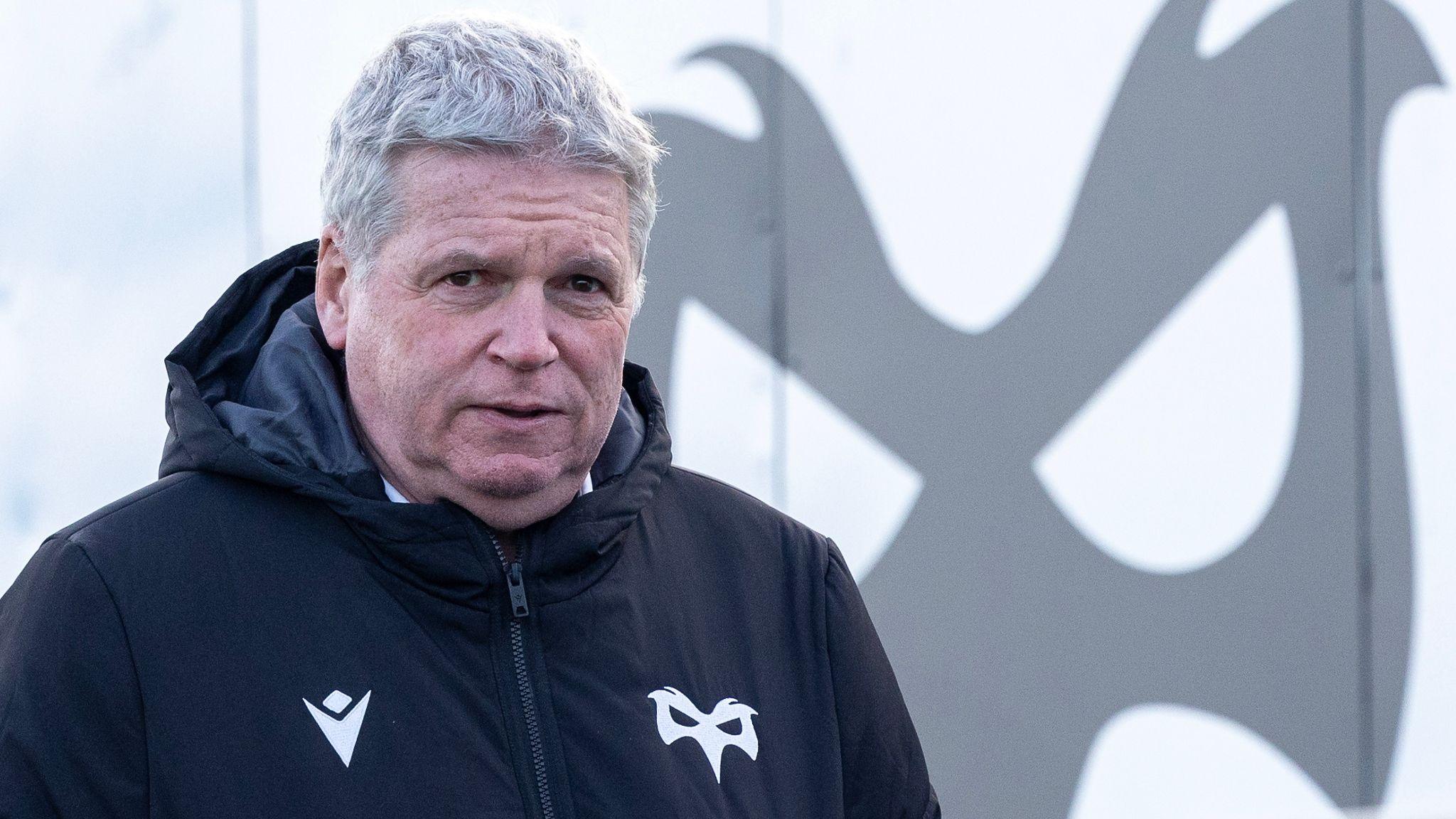 Lance Bradley wearing an Ospreys jacket in front of an Ospreys logo at Brewery Field