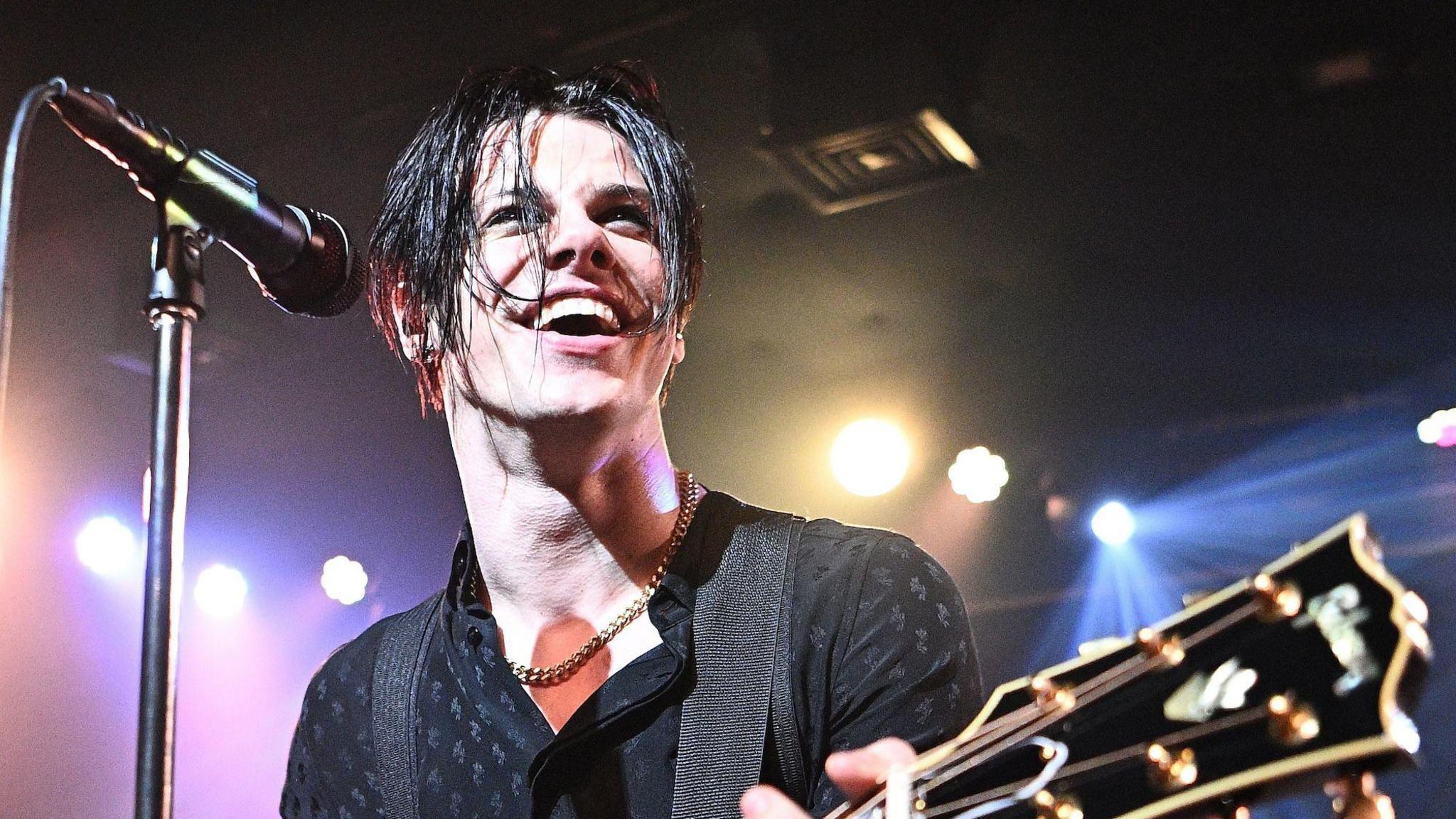 Yungblud smiles as he plays an acoustic guitar on stage in London, March 2025.