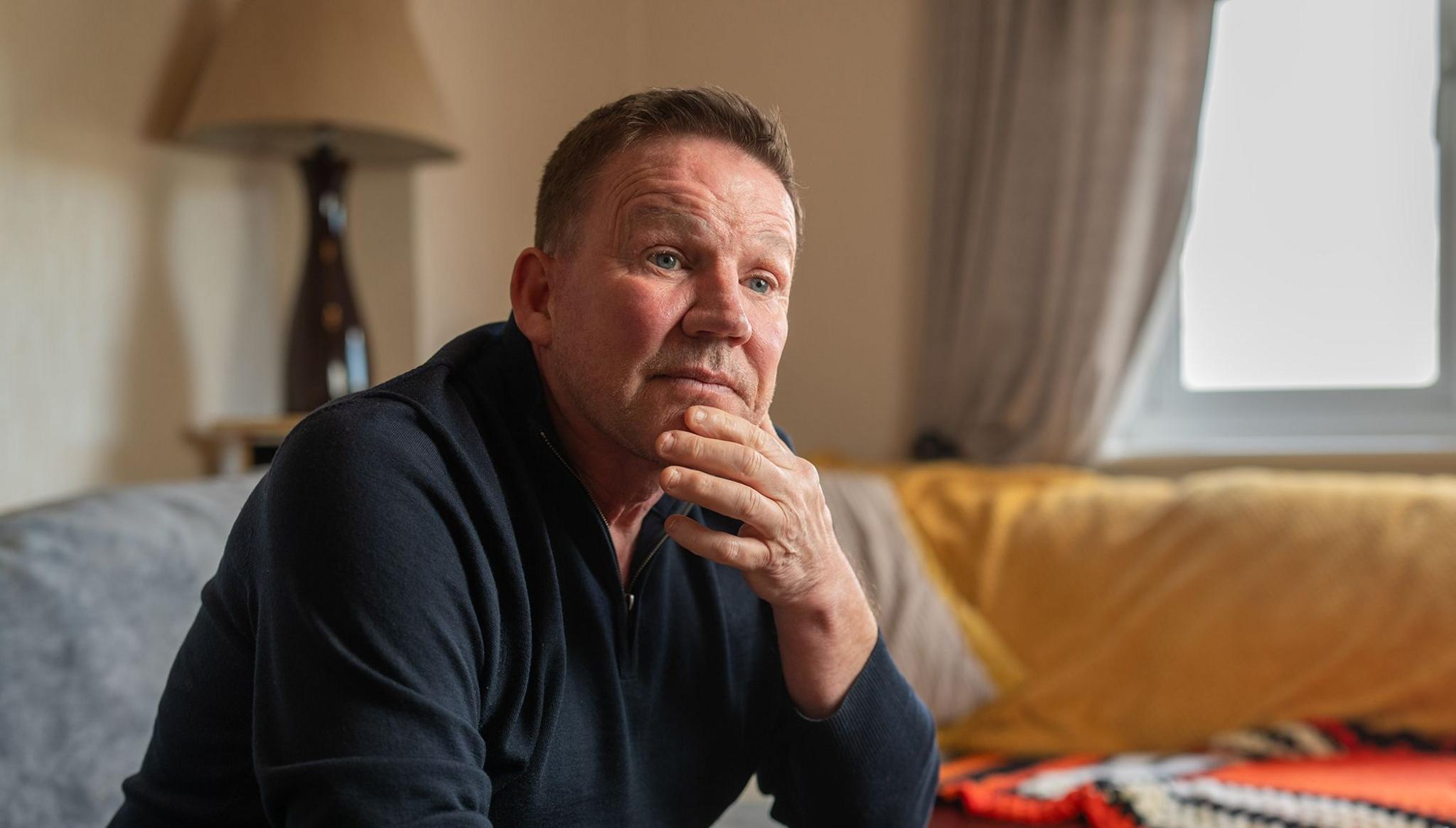 A man in a dark shirt sits on a sofa. 