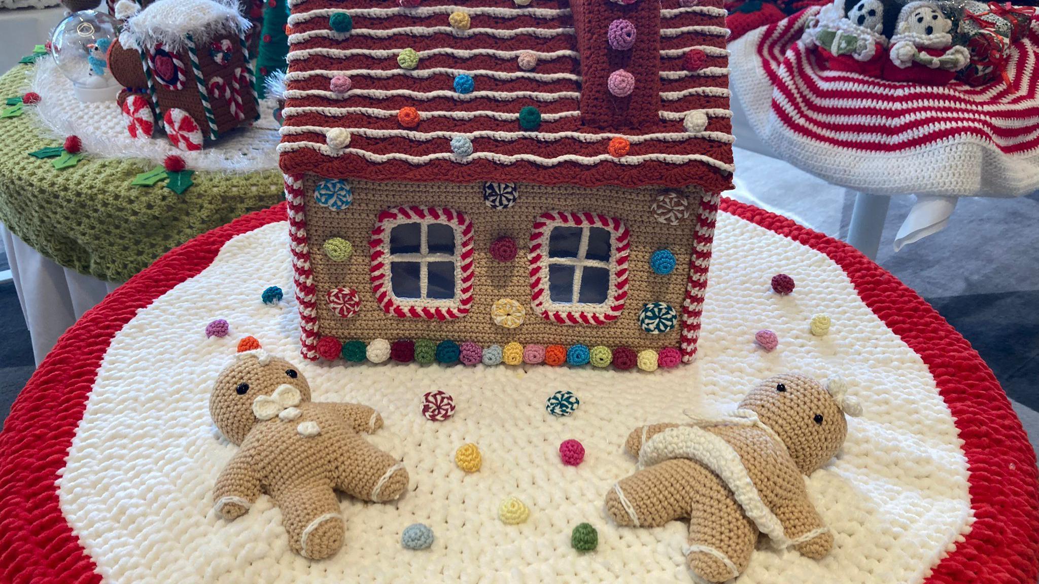 A post box topper in red and white decorated with two gingerbread and a gingerbread house.