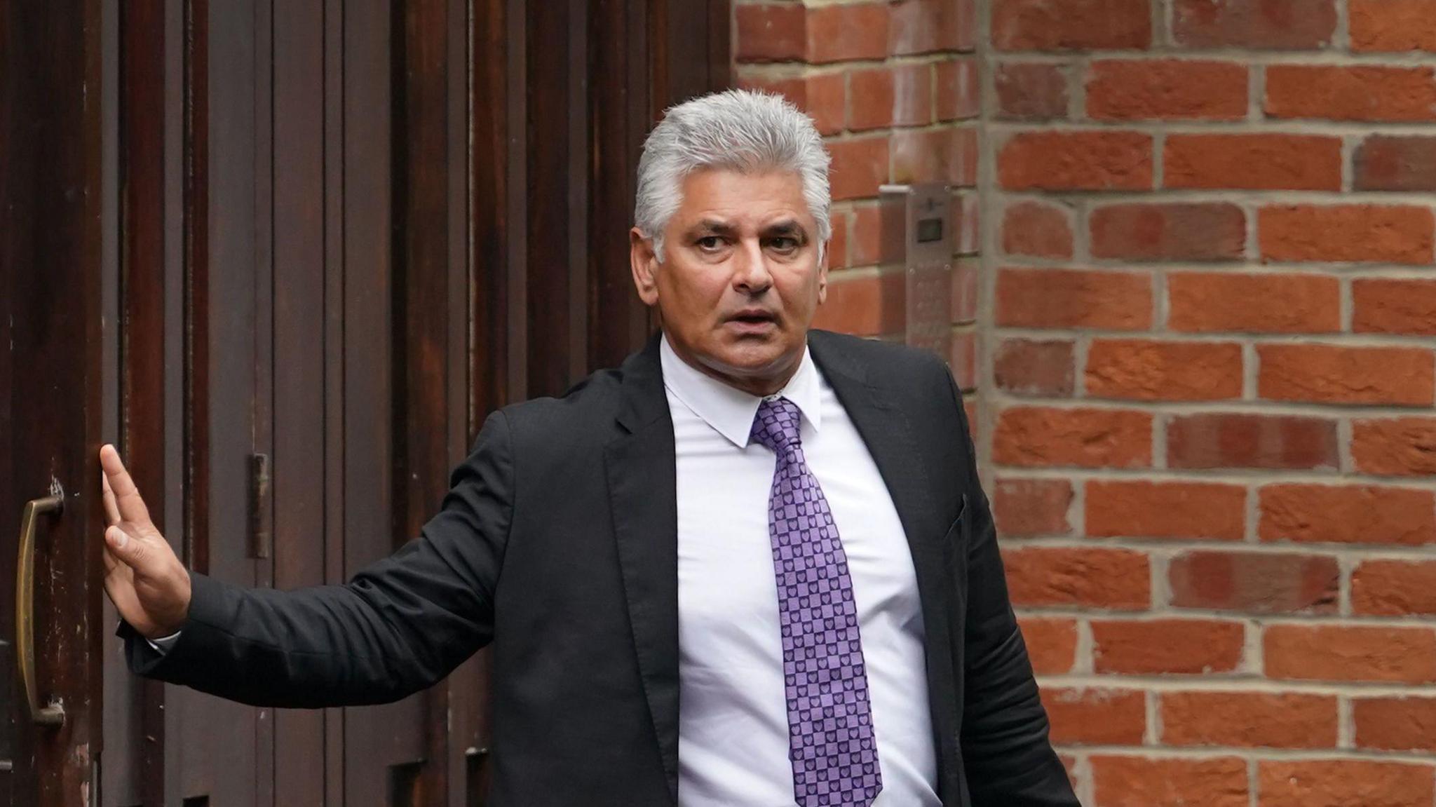 A man with a purple tie and blac suit exits a building.