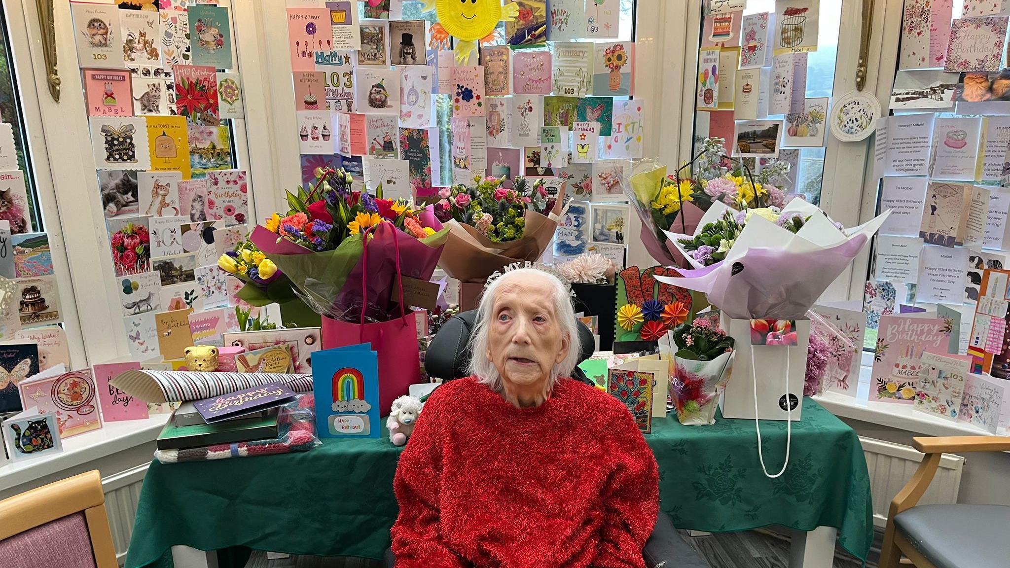 An image of an elderly lady sat in front of hundreds of birthday cards