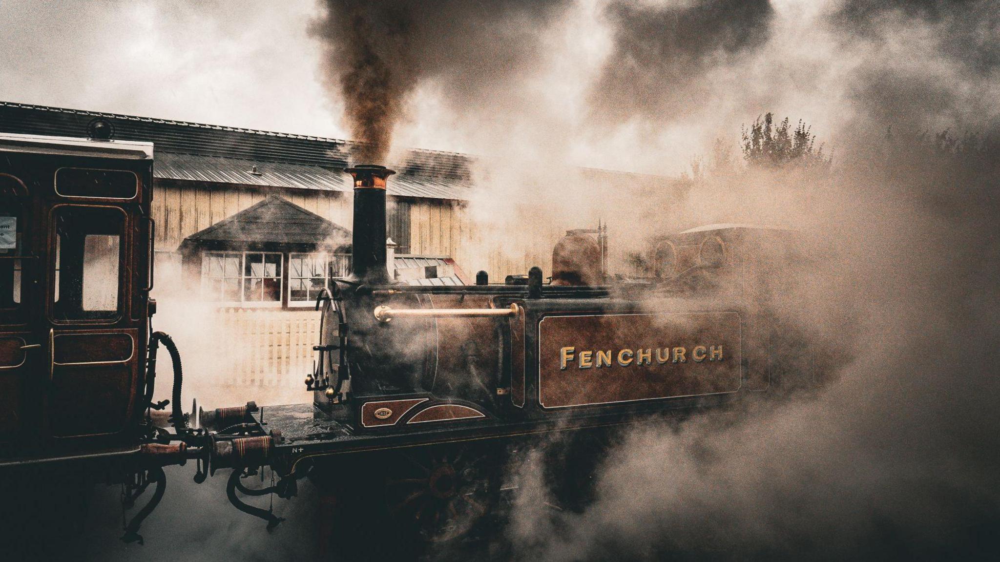 A red steam train in full steam at a station